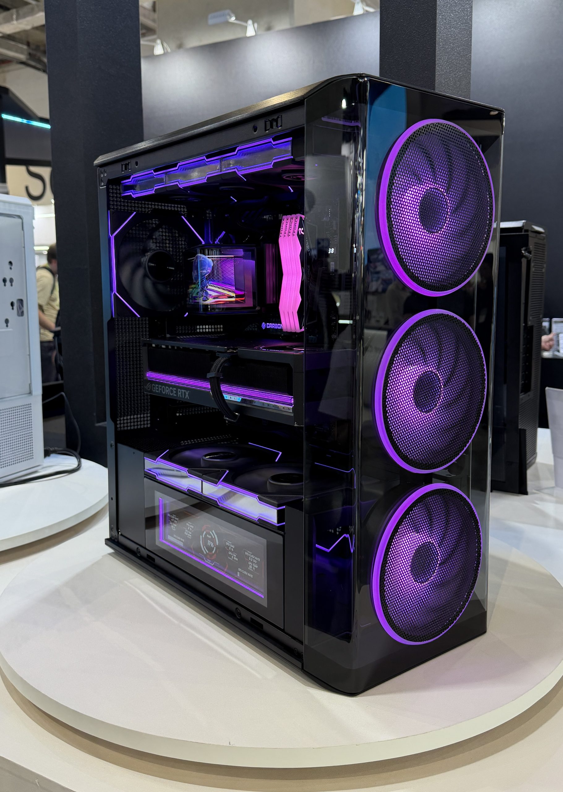 A high-performance gaming PC featuring a GeForce RTX graphics card and three large front fans with purple LED lighting.