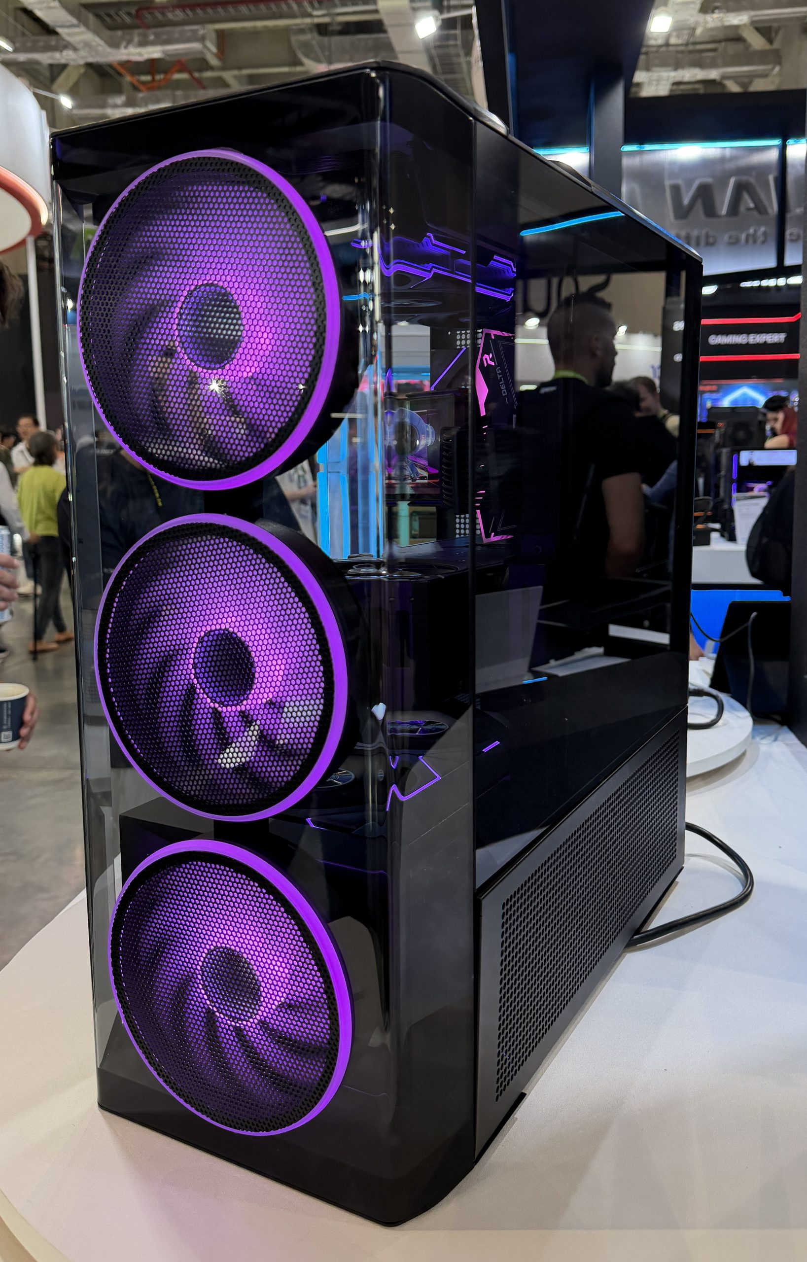 A custom-built gaming PC with a transparent case showcases three large purple LED fans at an exhibition.