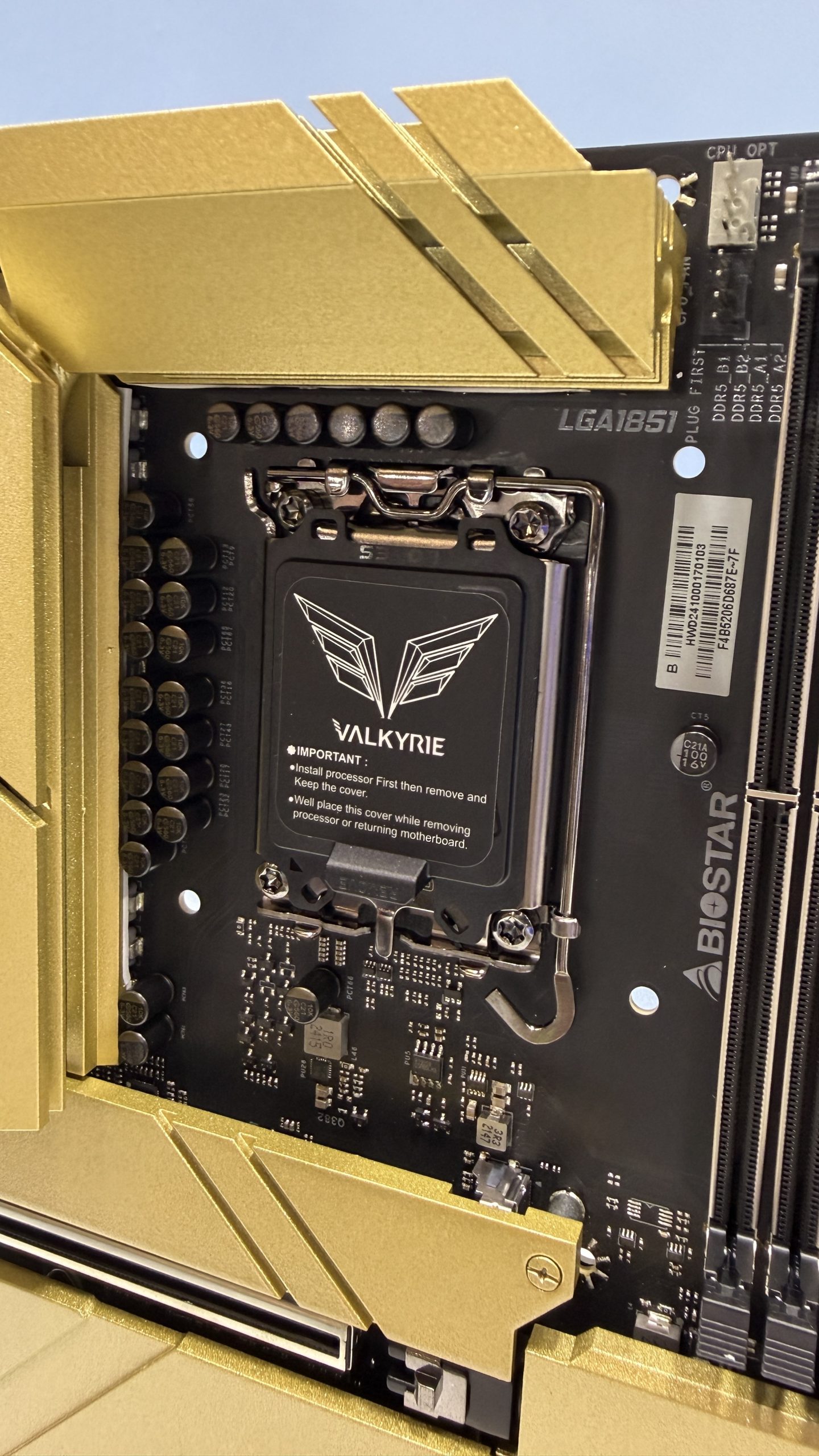 A Biostar motherboard features an LGA1851 socket with a 'VALKYRIE' cover, surrounded by gold accents and DDR5 memory slots.