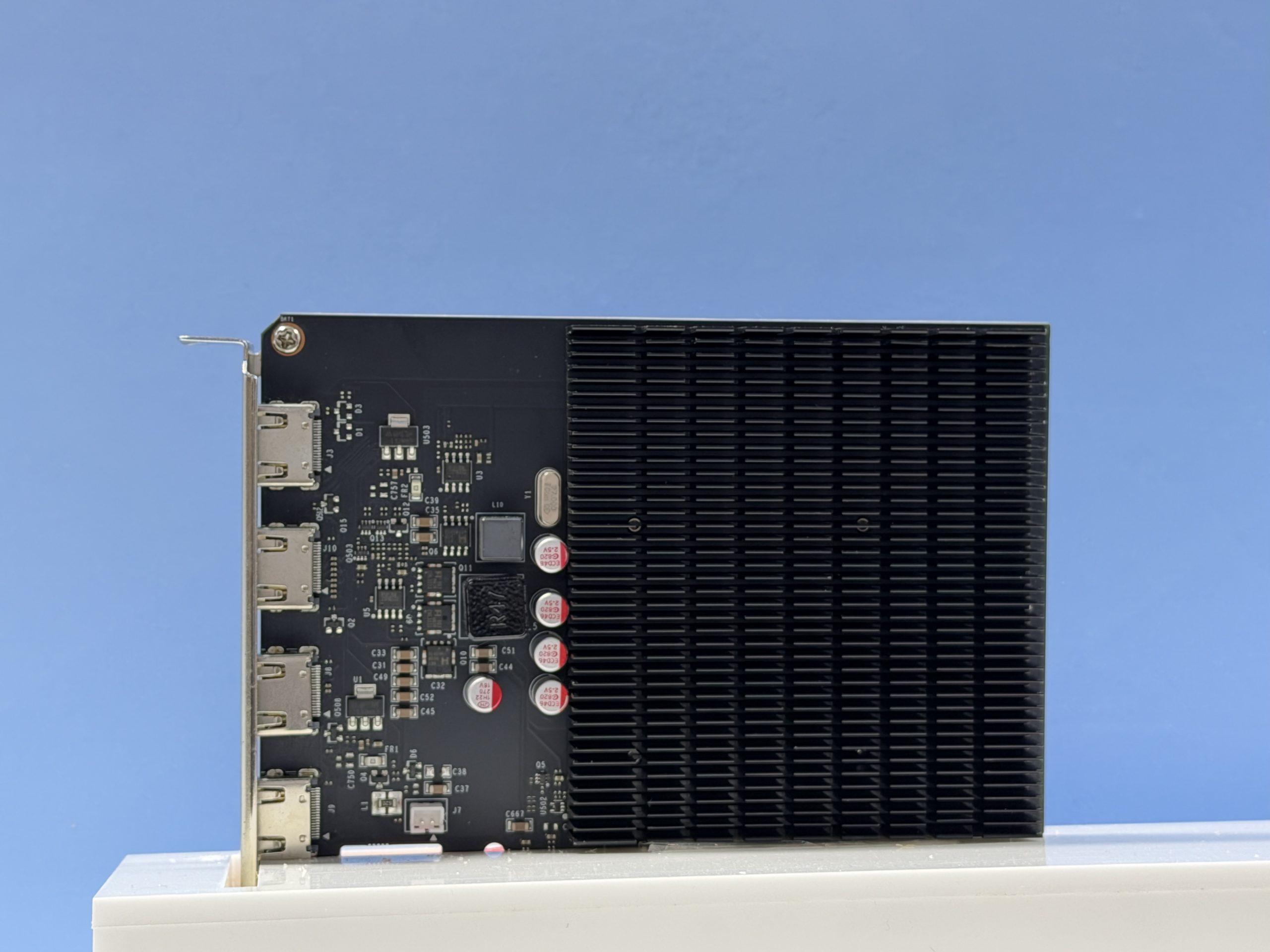 A fanless graphics card with three DisplayPort and one HDMI ports is displayed against a blue background.