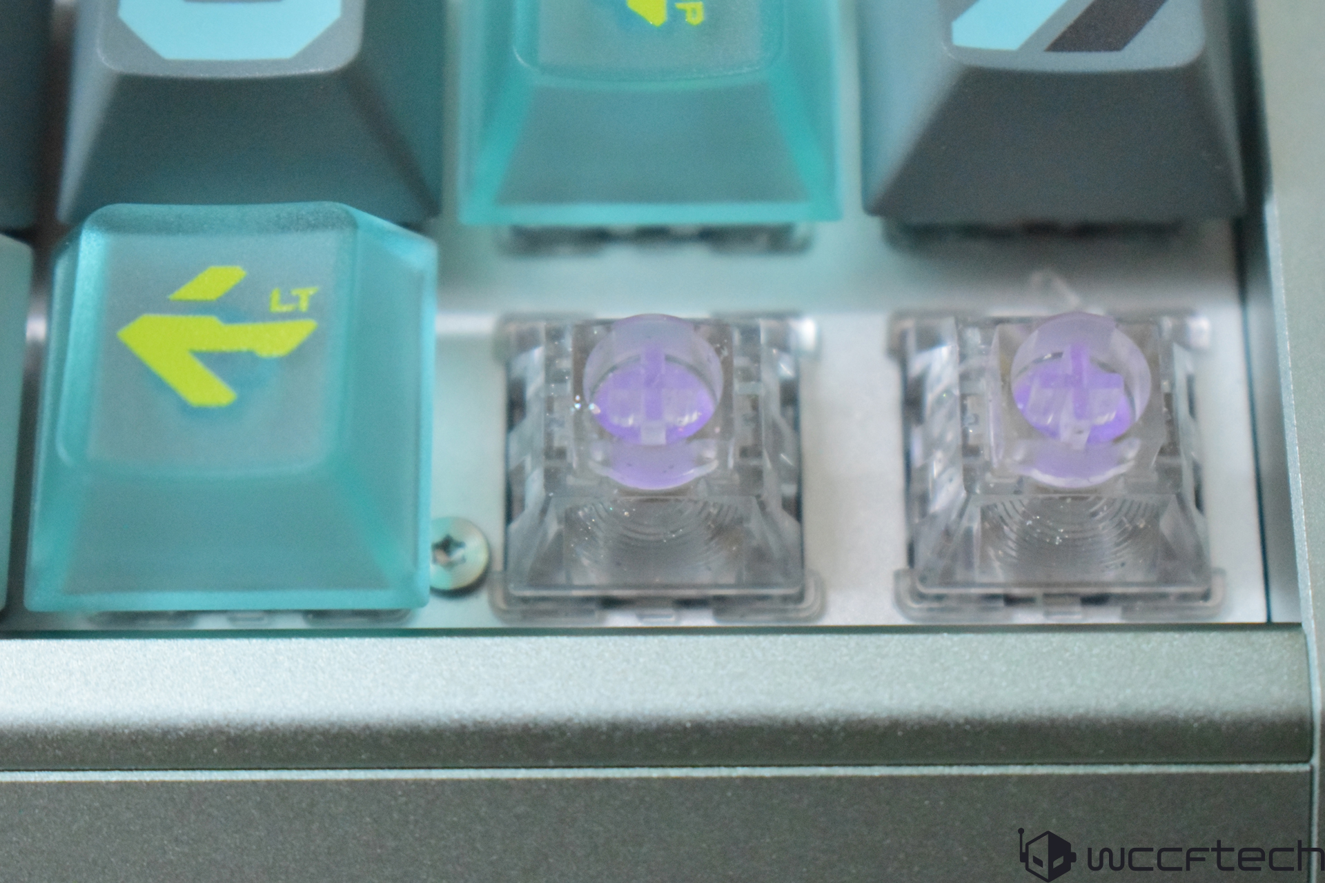 Transparent mechanical keyboard switches with purple stems are positioned between teal keycaps marked with yellow arrows and 'LT' text.