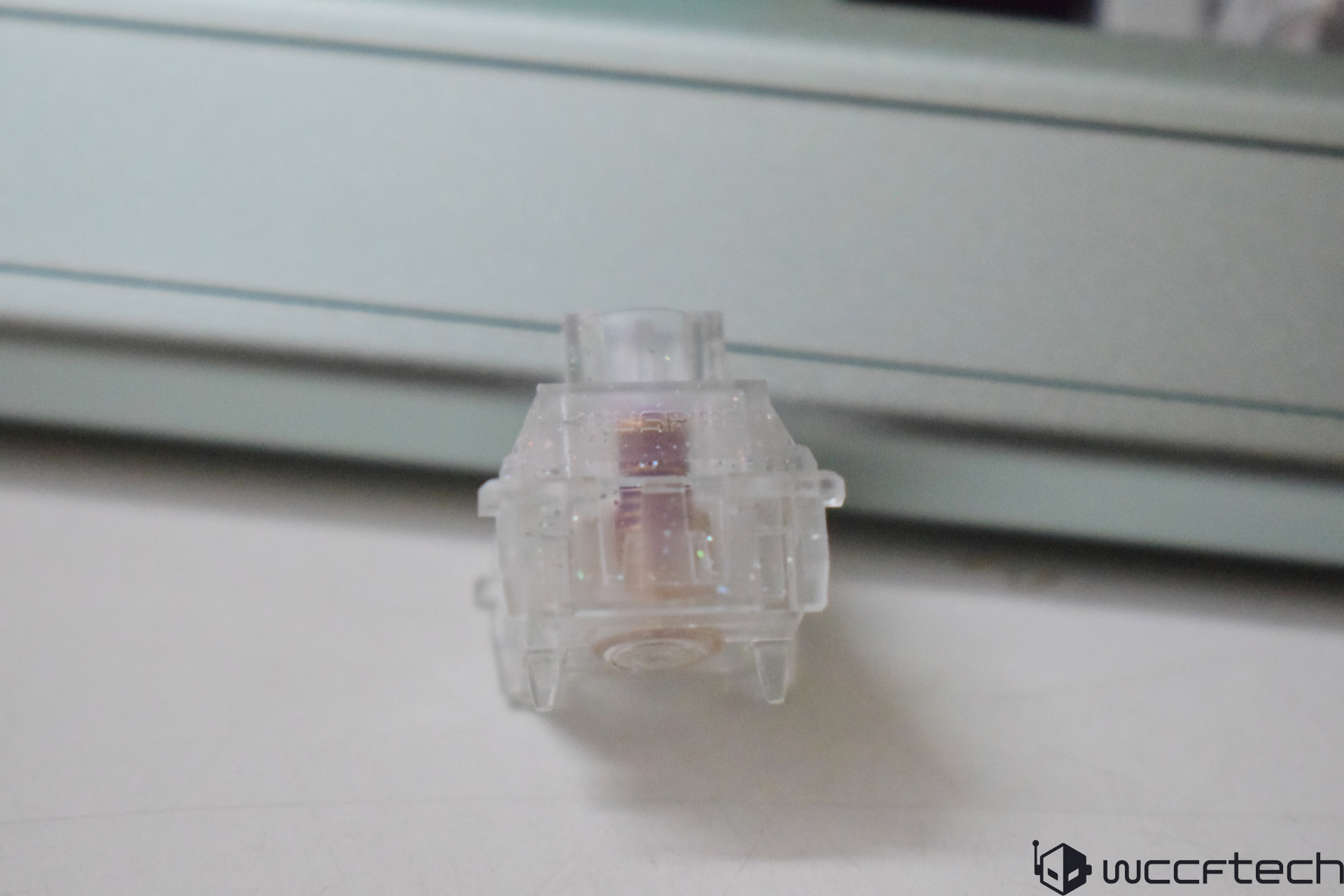 A close-up of a translucent mechanical keyboard switch with visible speckles, set against a blurred background.