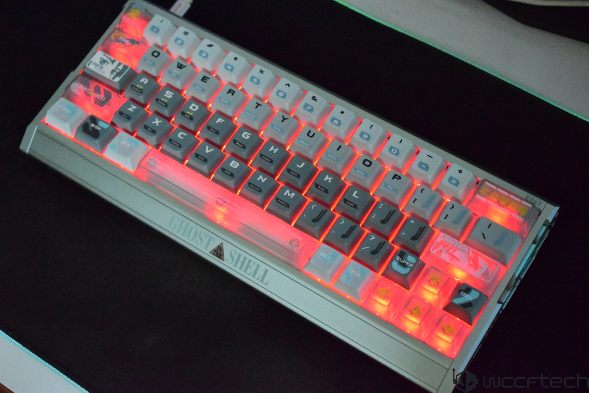A backlit keyboard with a Ghost in the Shell theme displays custom keycaps and red glowing lights.
