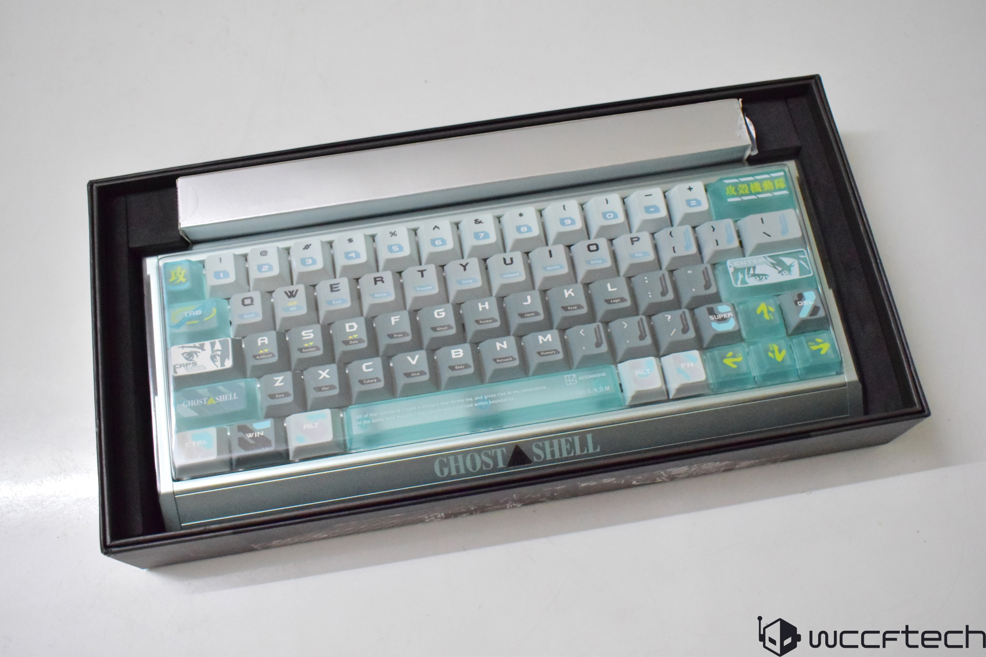 A Ghost in the Shell themed mechanical keyboard with blue and gray keycaps is presented in its packaging.