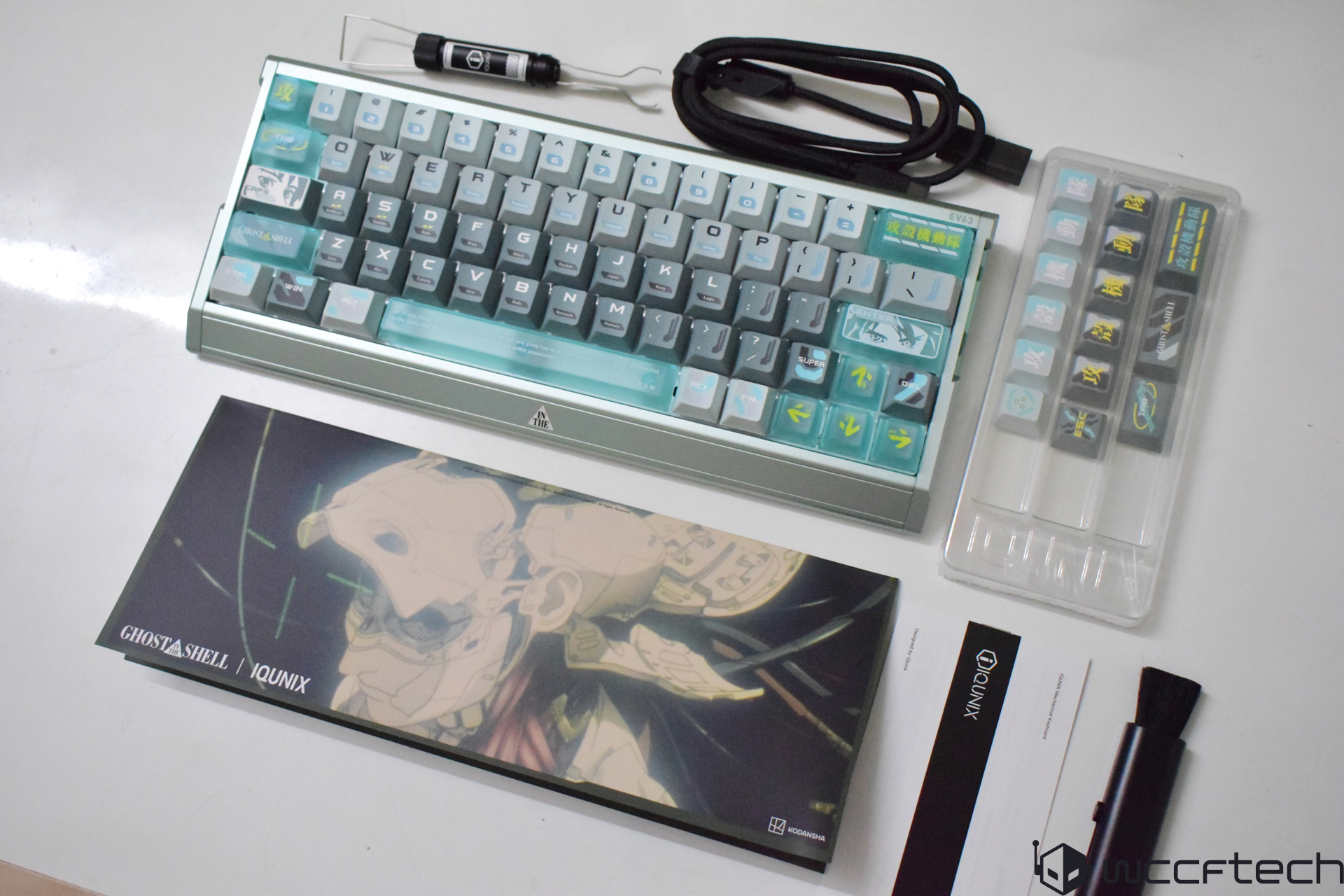 A IQUINIX Ghost in the Shell-themed mechanical keyboard with custom keycaps and additional accessories displayed on a table.