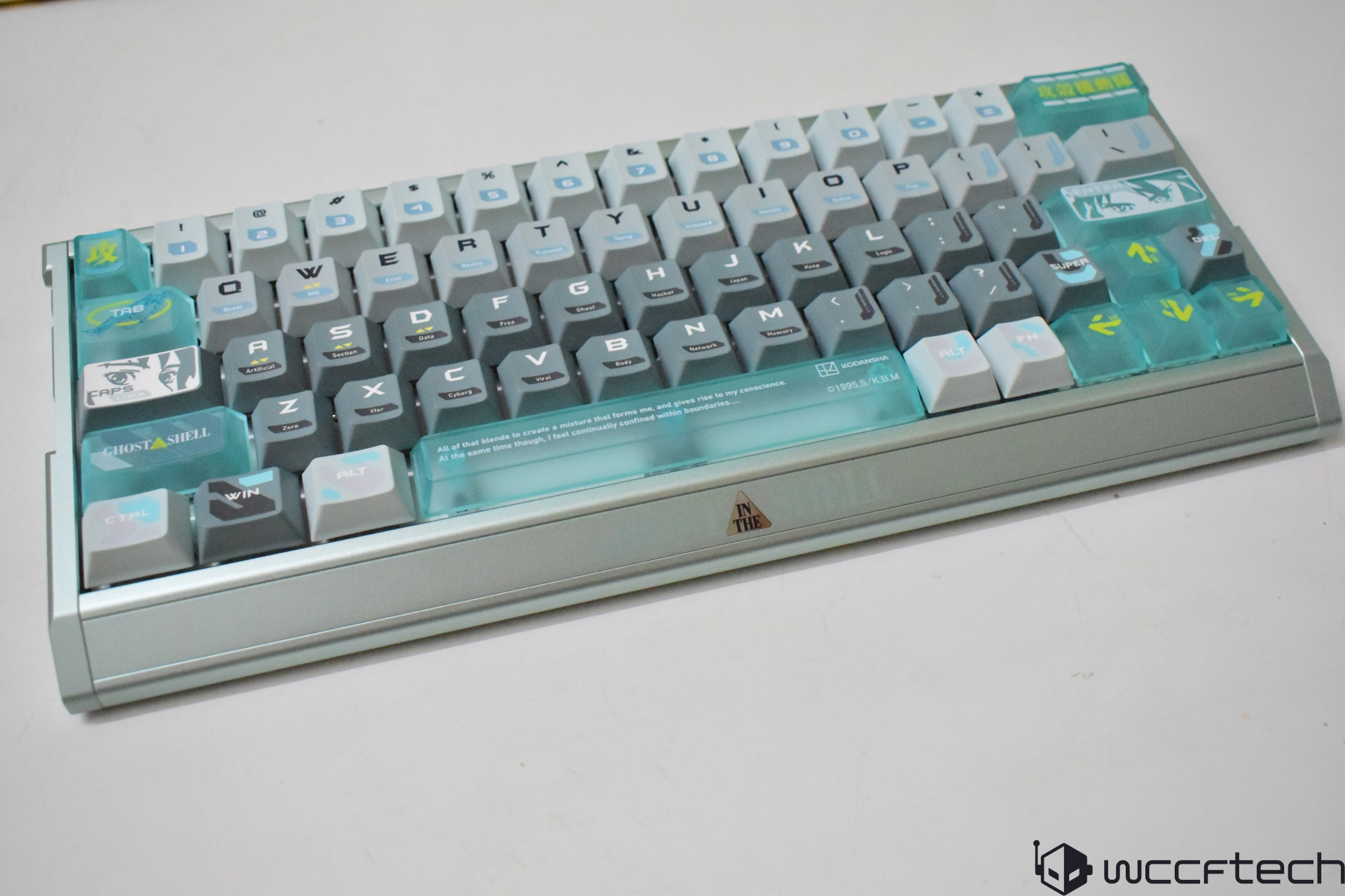 A compact mechanical keyboard with customized keycaps featuring themes such as 'GHOST IN THE SHELL' and various symbols, set on a metallic base with the logo IN THE.