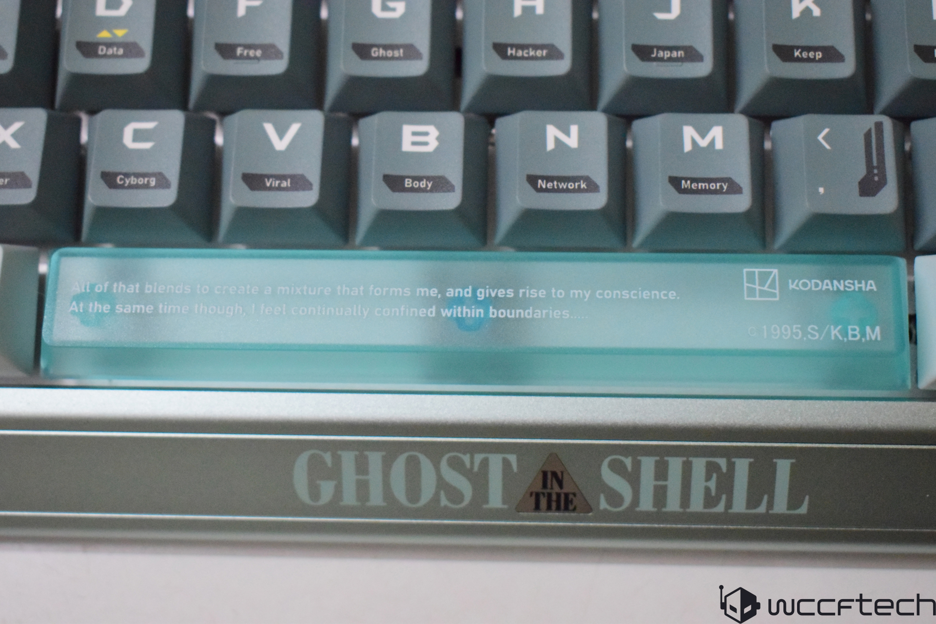 A custom keyboard features modified keycaps and a spacebar with text from 'Ghost in the Shell,' alongside the Kodansha logo and copyright information.