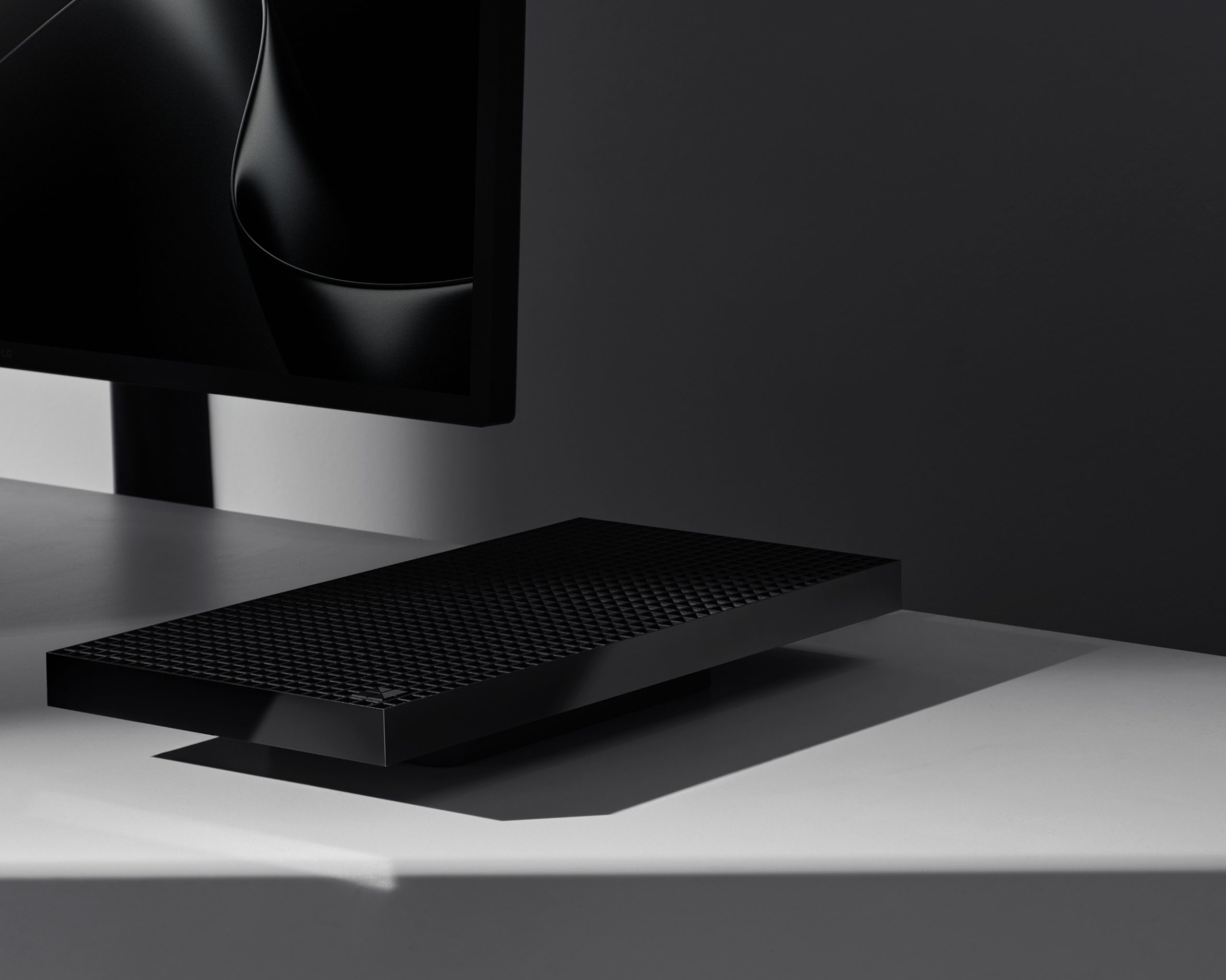A sleek black external hard drive with a textured surface is placed on a white desk beside the lower corner of a monitor.