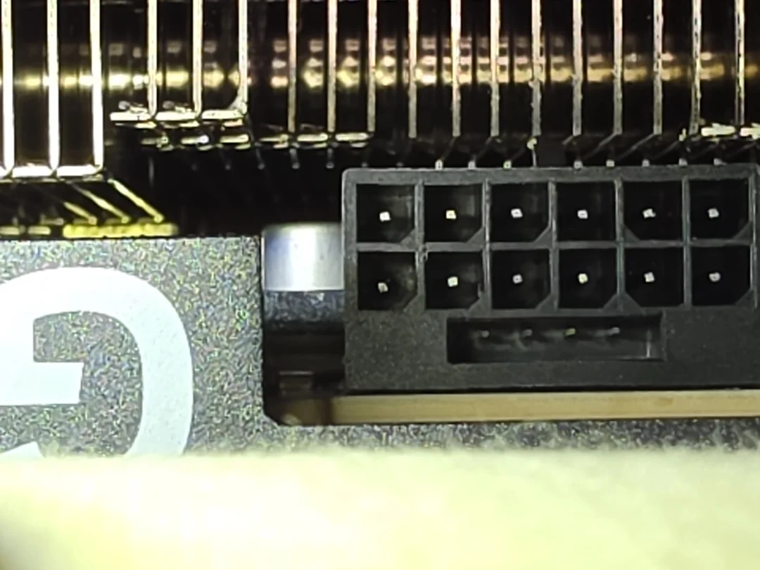 A close-up view of a GPU power connector showcasing a 16-pin interface next to metallic cooling fins, with a partially visible 'G' logo on the card's casing.