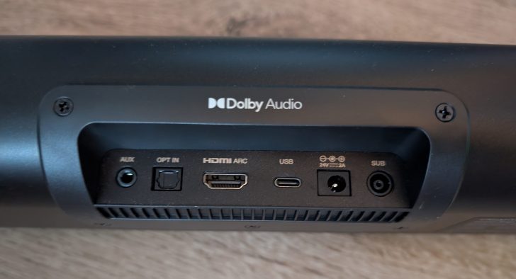 The image shows the back panel of a soundbar featuring Dolby Audio branding, with visible ports labeled 'AUX,' 'OPT IN,' 'HDMI ARC,' 'USB,' '24V⎓⎓-2A,' and 'SUB.'