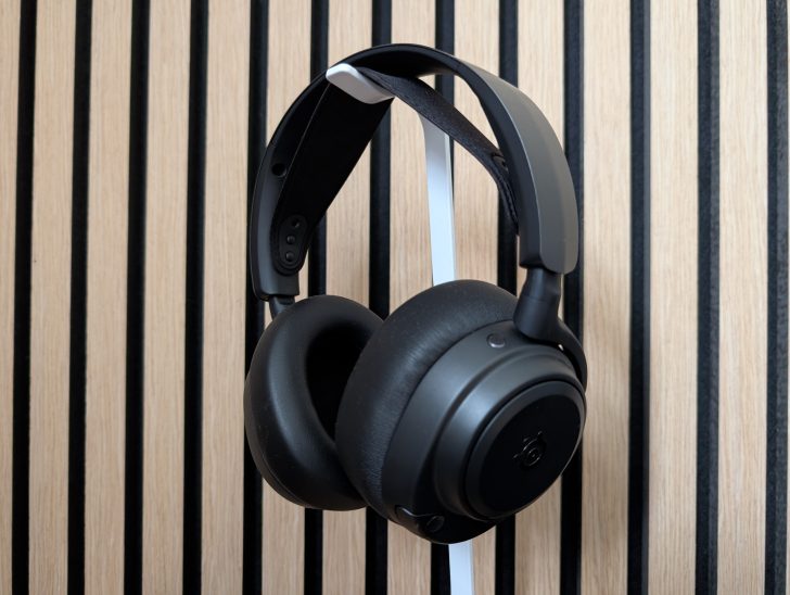 A pair of SteelSeries Arctis Nova Pro headphones hangs in front of a wooden slatted wall.