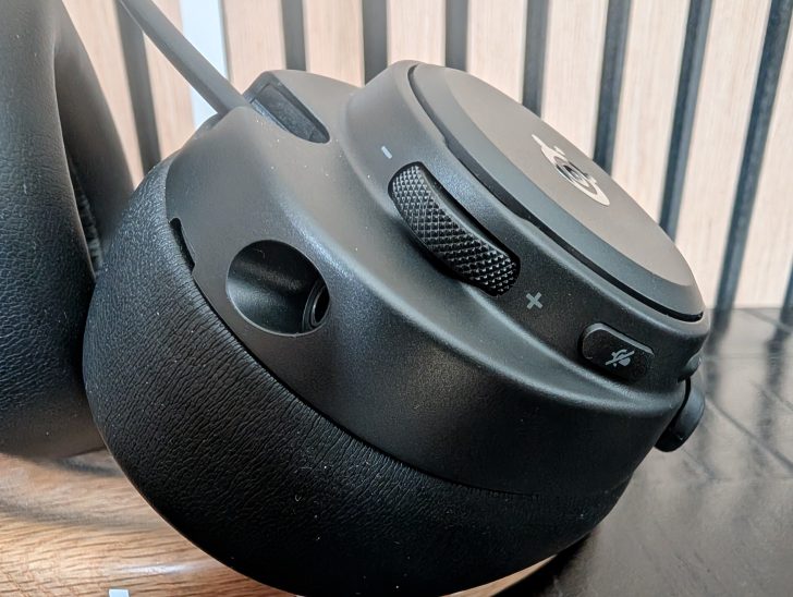 A close-up of the SteelSeries logo on a black gaming headset with visible volume dial and mute button.