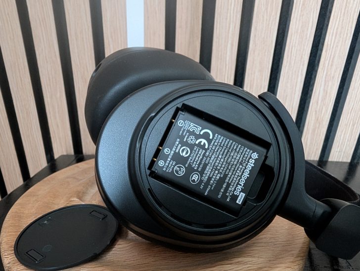 A SteelSeries Arctis headset with the battery compartment open, showing the battery labeled 'SteelSeries.'