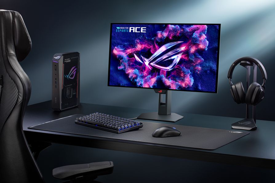An ASUS ROG gaming setup featuring a monitor displaying the ROG logo with the text 'MADE FOR ESPORTS ACE,' a keyboard, mouse, headset, and a boxed ROG accessory on a desk.