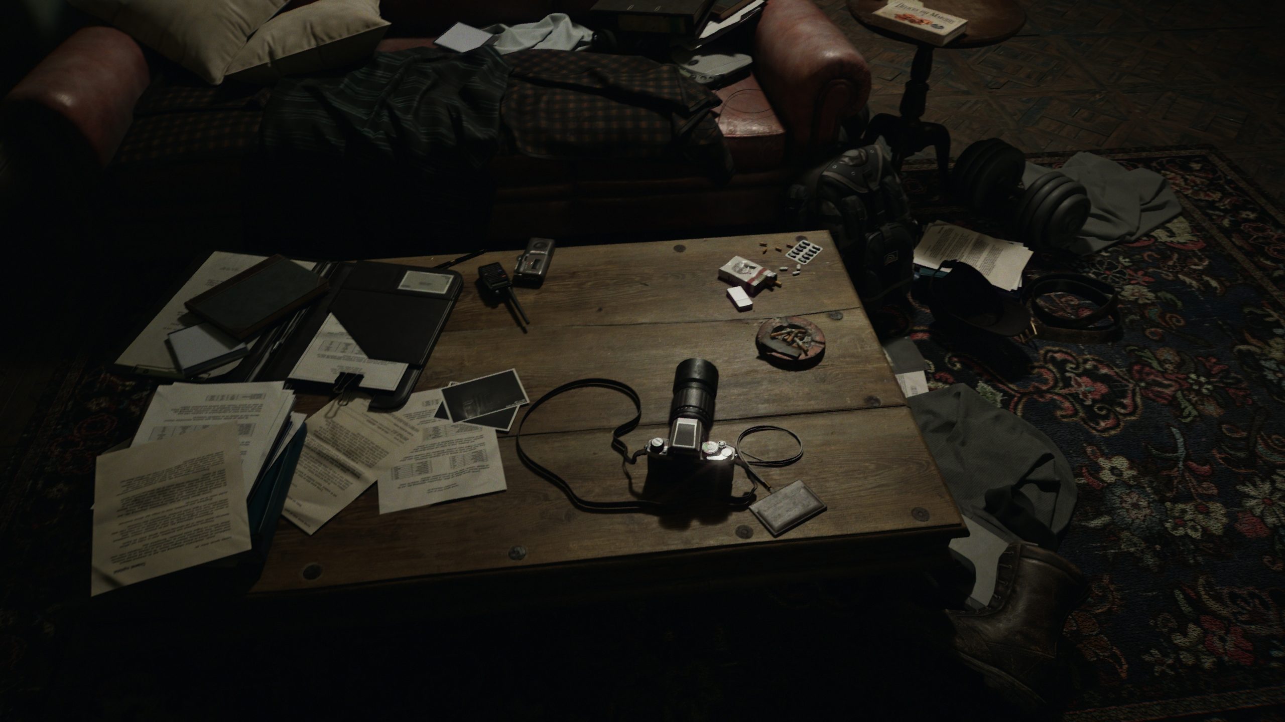 A cluttered table is filled with scattered documents, a vintage camera with a long lens, photographs, pills, and a leather wallet, set in a dimly lit room with a leather sofa and patterned rug.