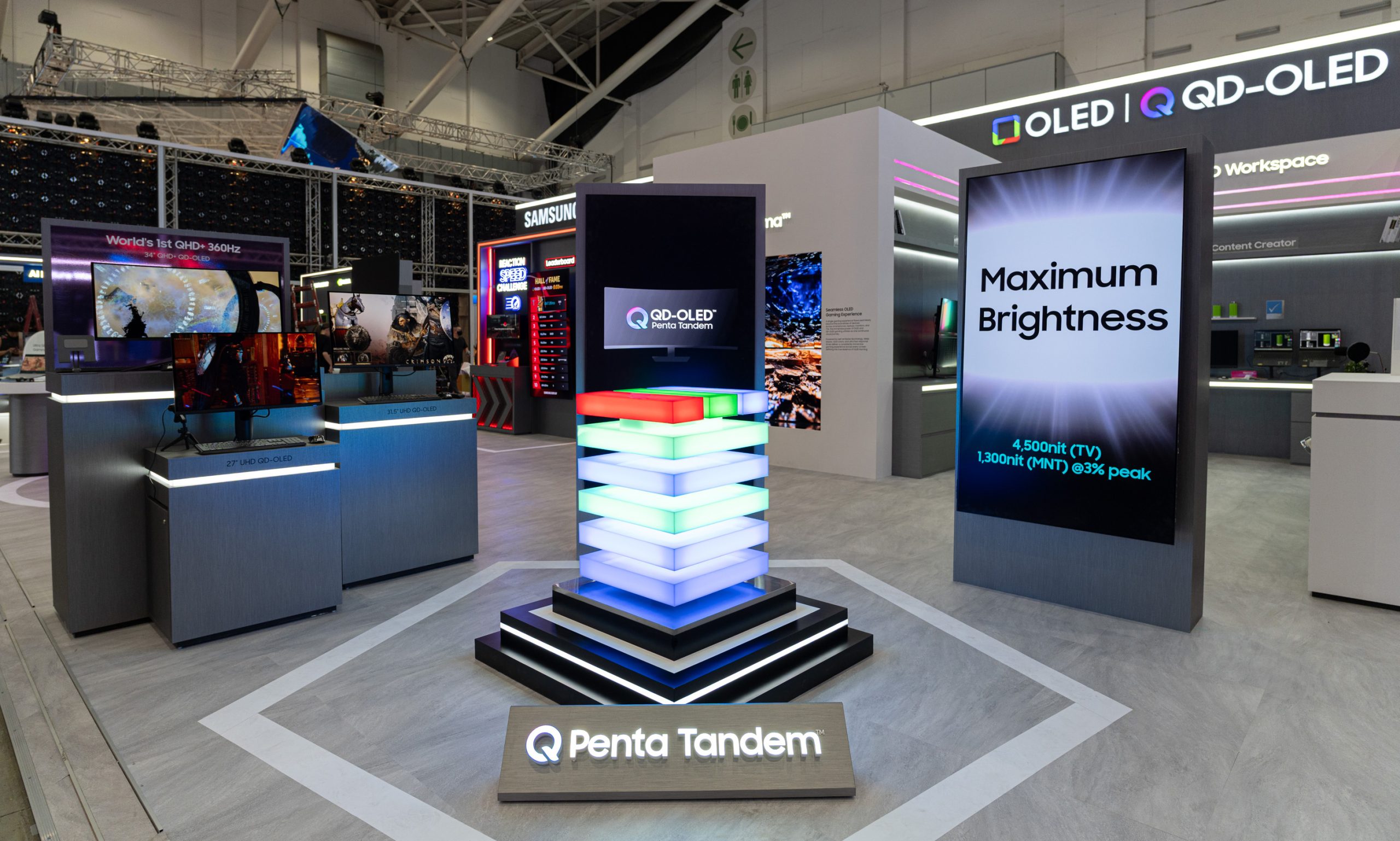 A display at a tech exhibition showcases Samsung's QD-OLED Penta Tandem technology alongside monitors labeled '27 UHD QD-OLED' and '34 QHD QD-OLED 360Hz,' with a screen advertising 'Maximum Brightness' of '4,500nit (TV)' and '1,300nit (MNT) @3% peak.'