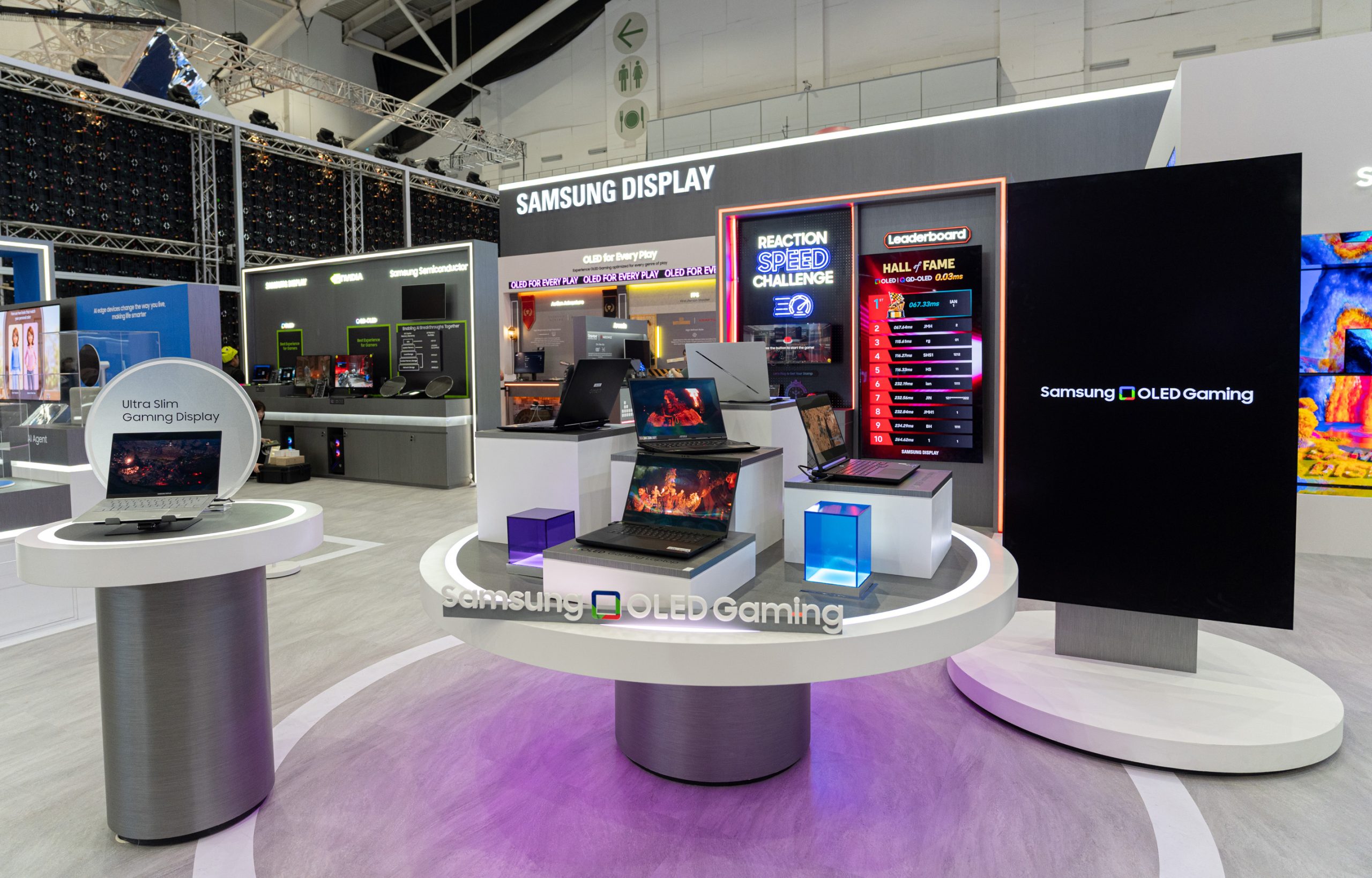 A Samsung Display booth showcases a variety of laptops featuring 'Ultra Slim Gaming Display' technology, highlighted by a leaderboard titled 'Reaction Speed Challenge' and a sign for 'Samsung OLED Gaming.'