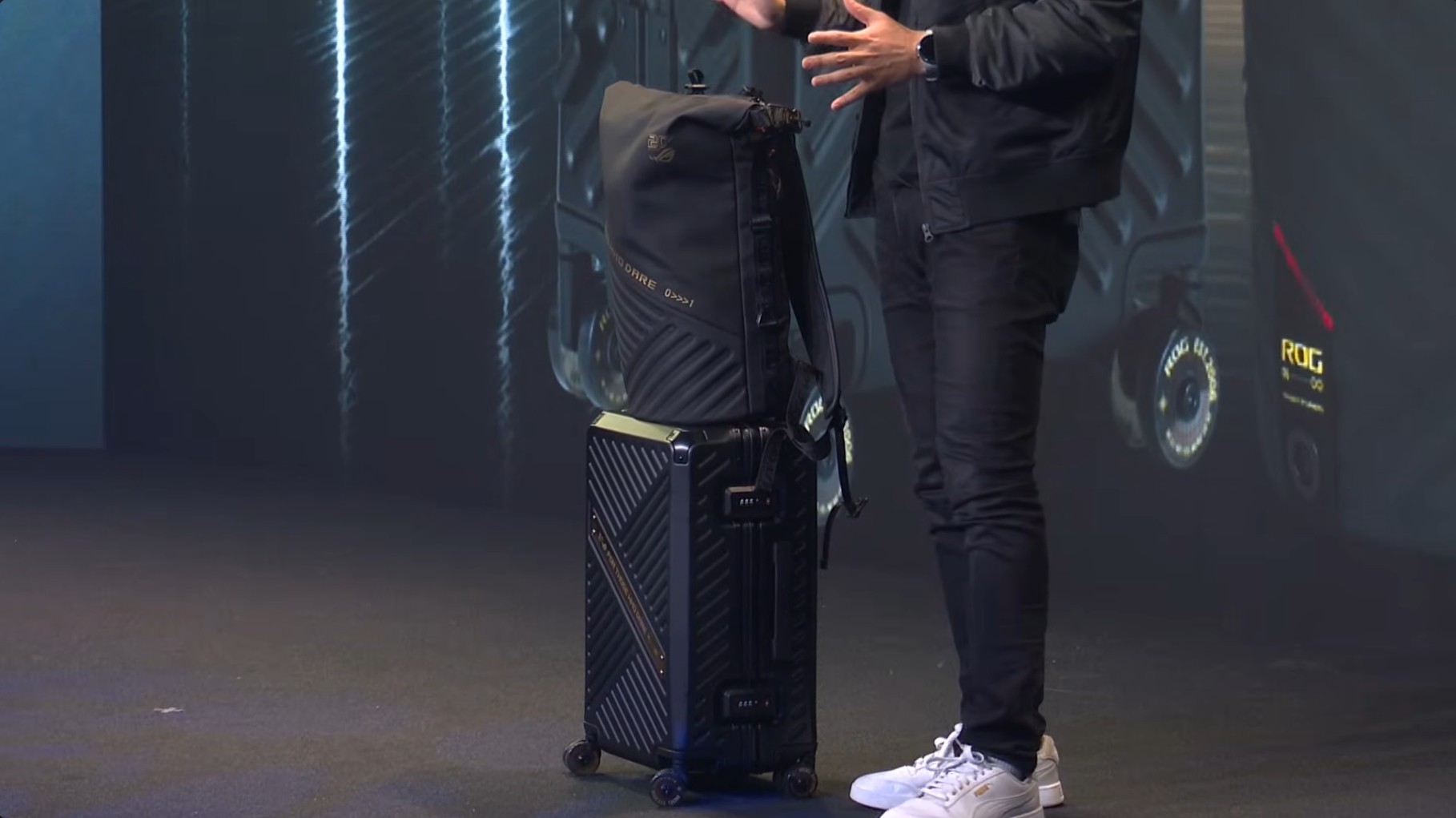 A person standing next to an ASUS ROG-branded backpack and suitcase on a stage.