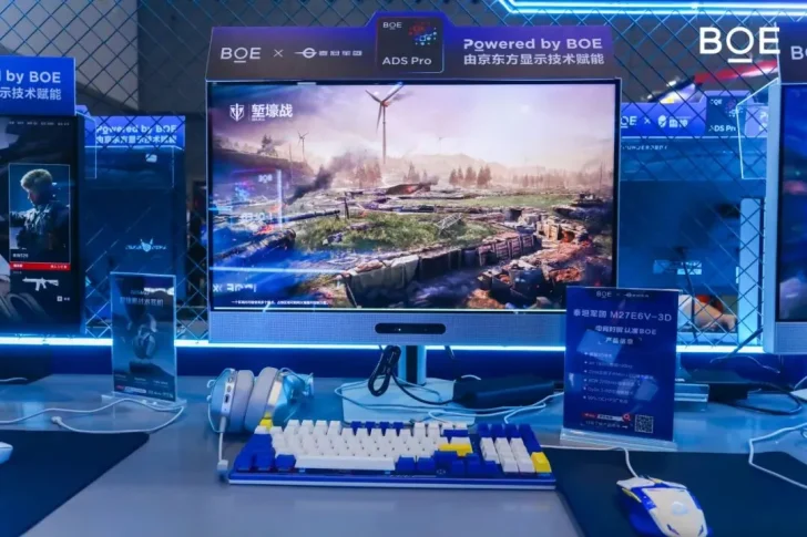 A BOE M27E6V-3D monitor displaying a game scene with wind turbines and trenches, surrounded by gaming peripherals.
