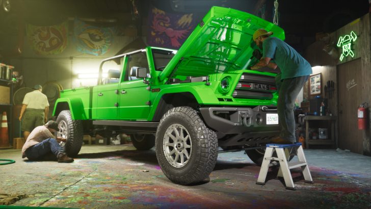A person works under the open hood of a bright green Canis 4x4 in a garage filled with tools and artistic decorations.