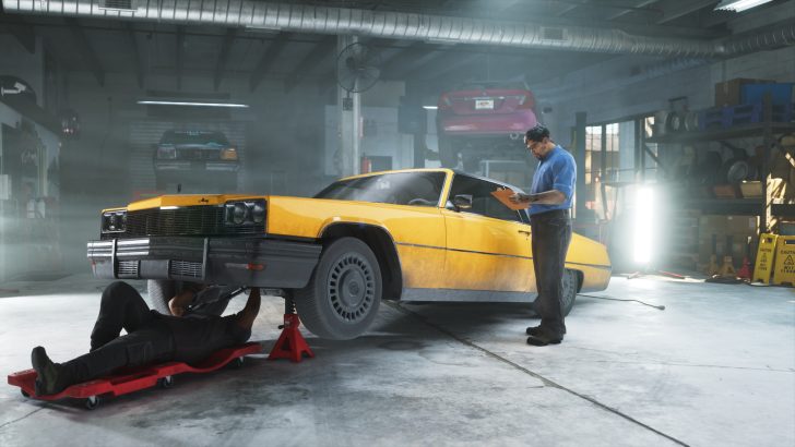 A mechanic works under a yellow car in a garage while another person reviews notes.