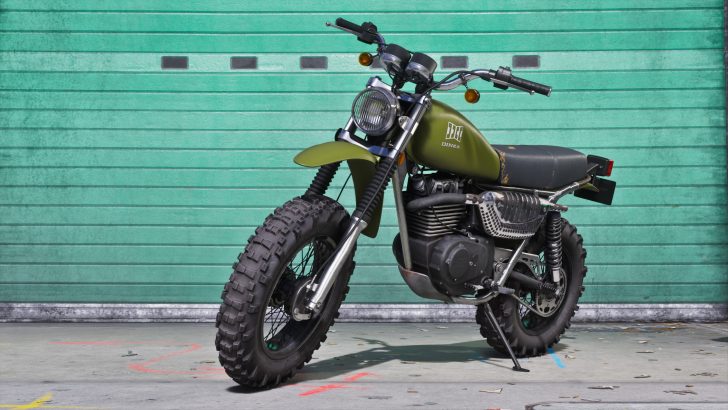 A green Dinka brand motorcycle is parked in front of a closed turquoise garage door.