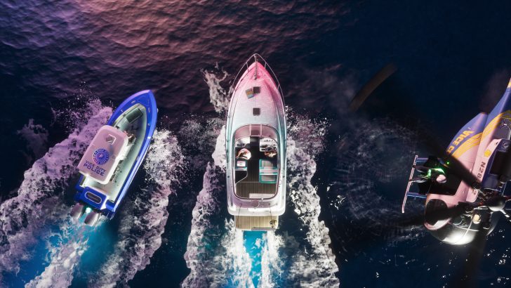 A luxury yacht in 'Grand Theft Auto V' is pursued by a 'VCPD Police' boat and a 'VICE CITY POLICE' helicopter over the ocean.
