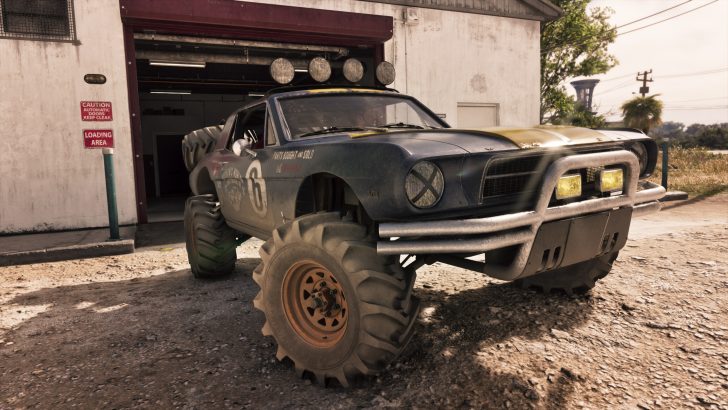 A rugged off-road vehicle with large tires and a number '6' on the side is parked outside an auto garage under a sign reading 'Loading Area.'