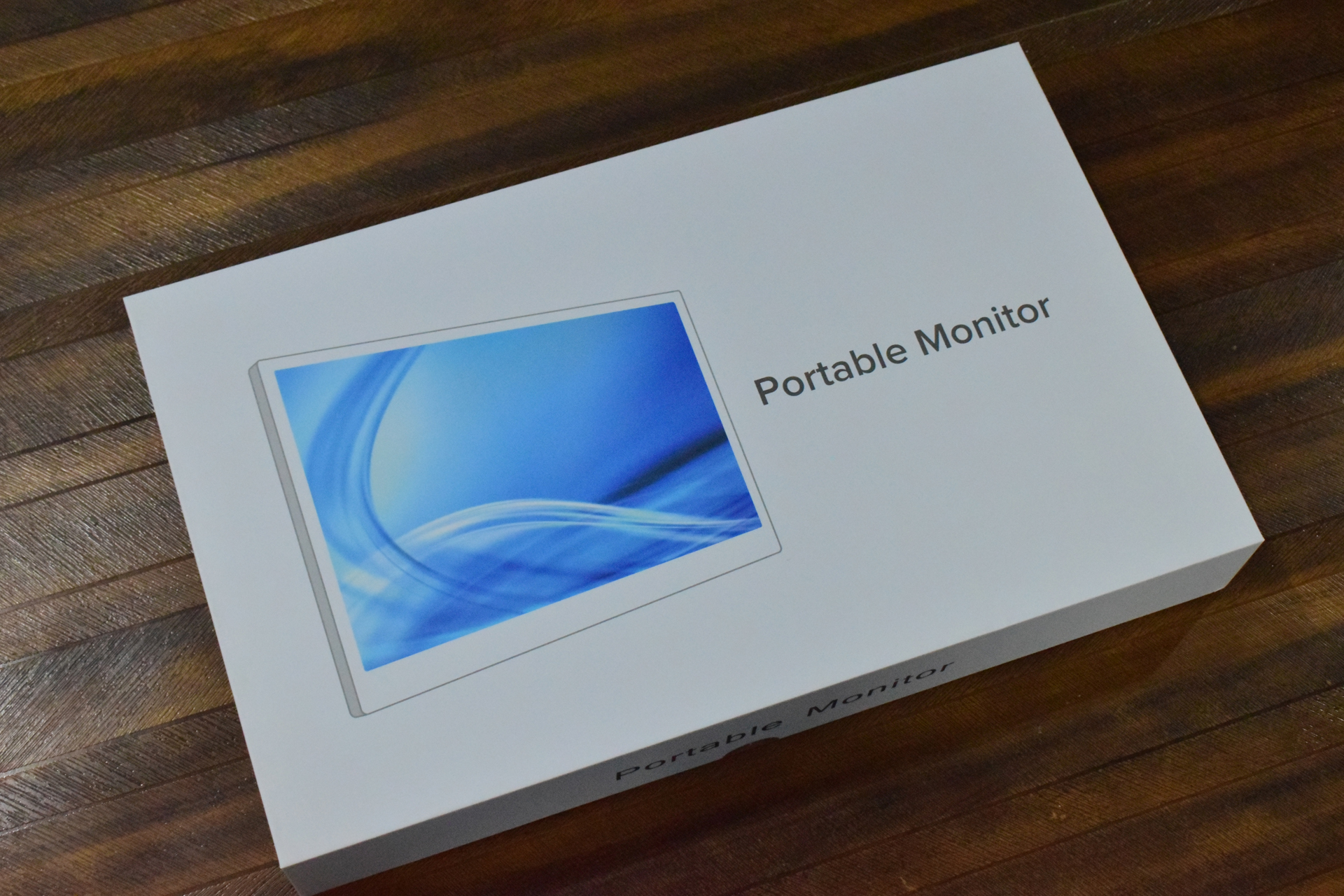 A box labeled 'Portable Monitor' is on a wooden surface, displaying an image of a monitor with a blue abstract design.