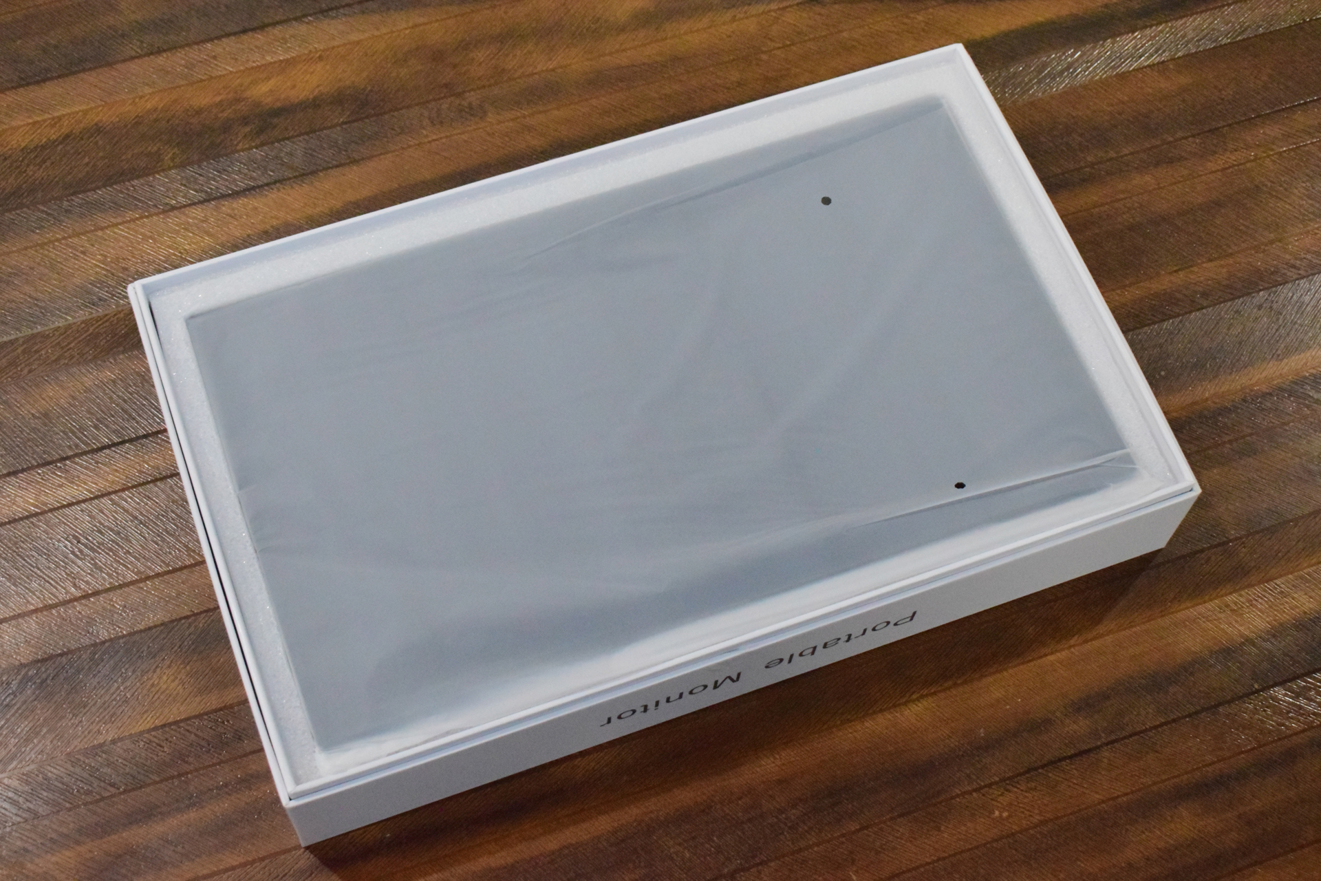 A portable monitor in a white box lies on a wooden surface.