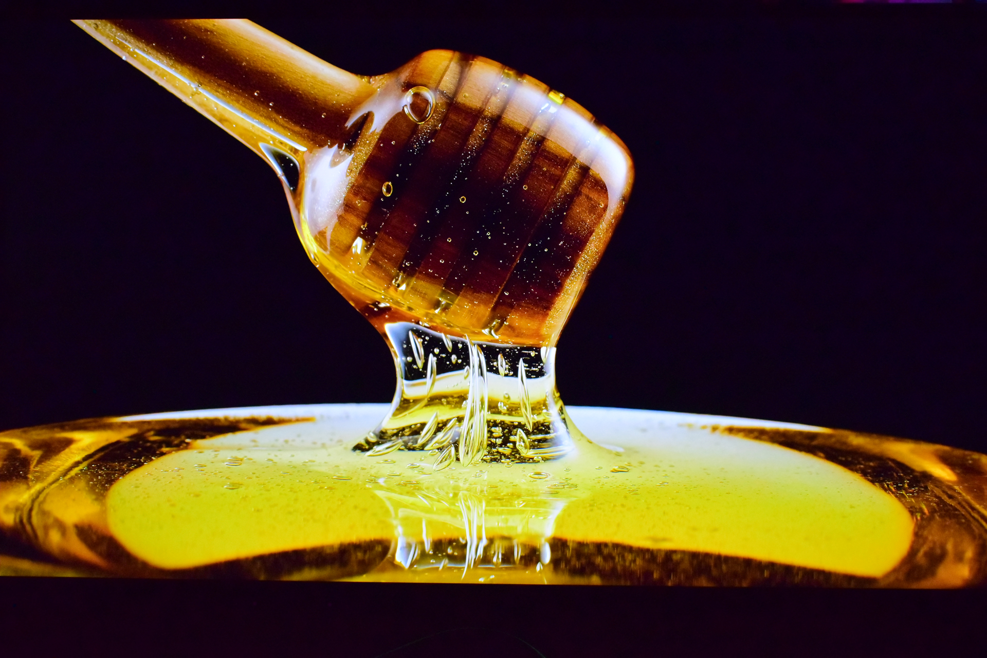 A close-up of a honey dipper dripping honey against a dark background.