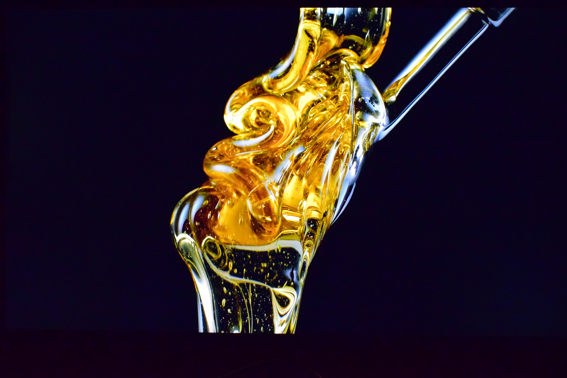Golden-hued liquid being poured against a black background, with swirling patterns and reflective highlights.