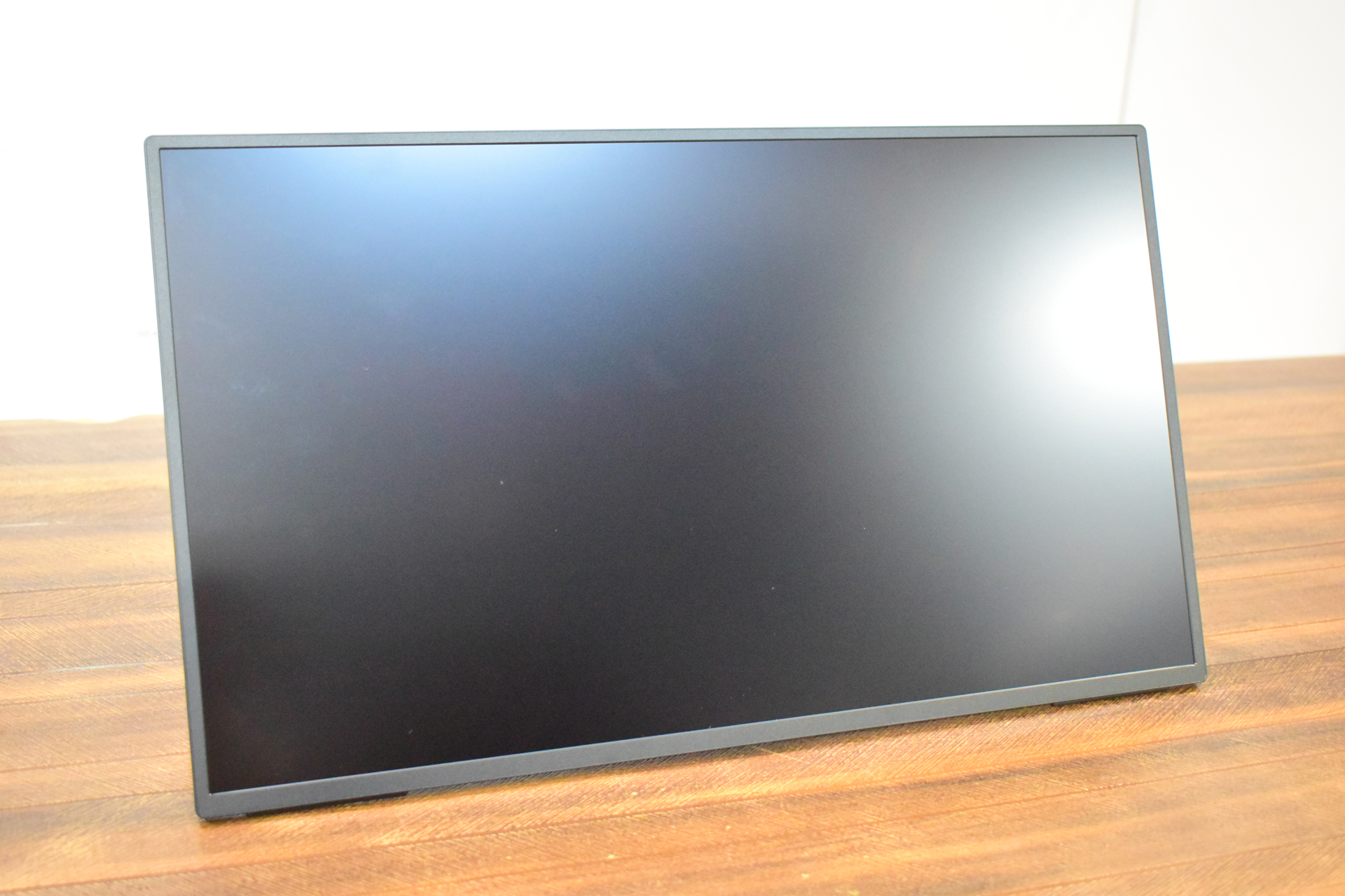 A matte-finish, bezel-less computer monitor with a black frame, placed on a wooden surface.