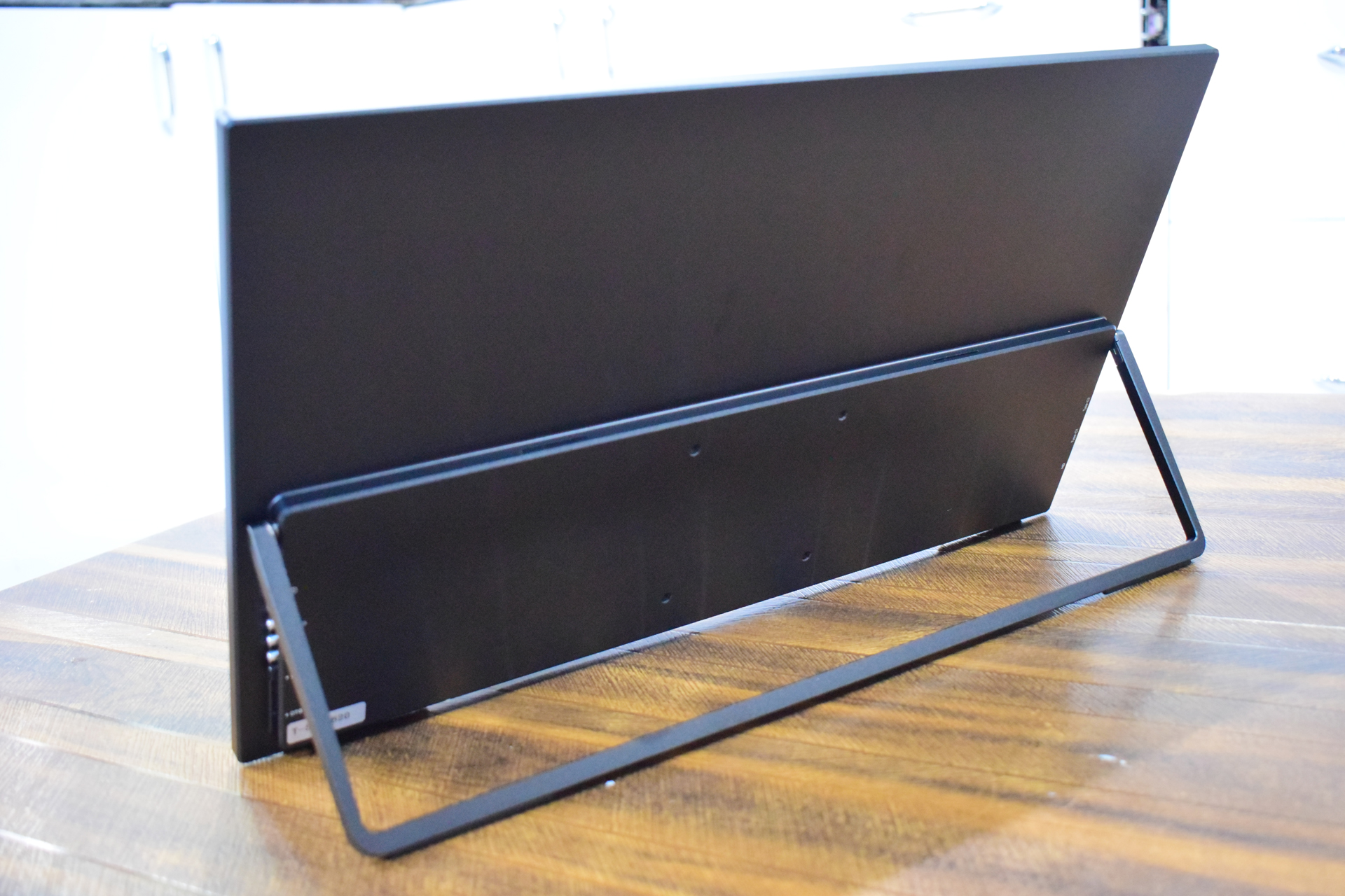 A black monitor with a stand is positioned on a wooden surface.