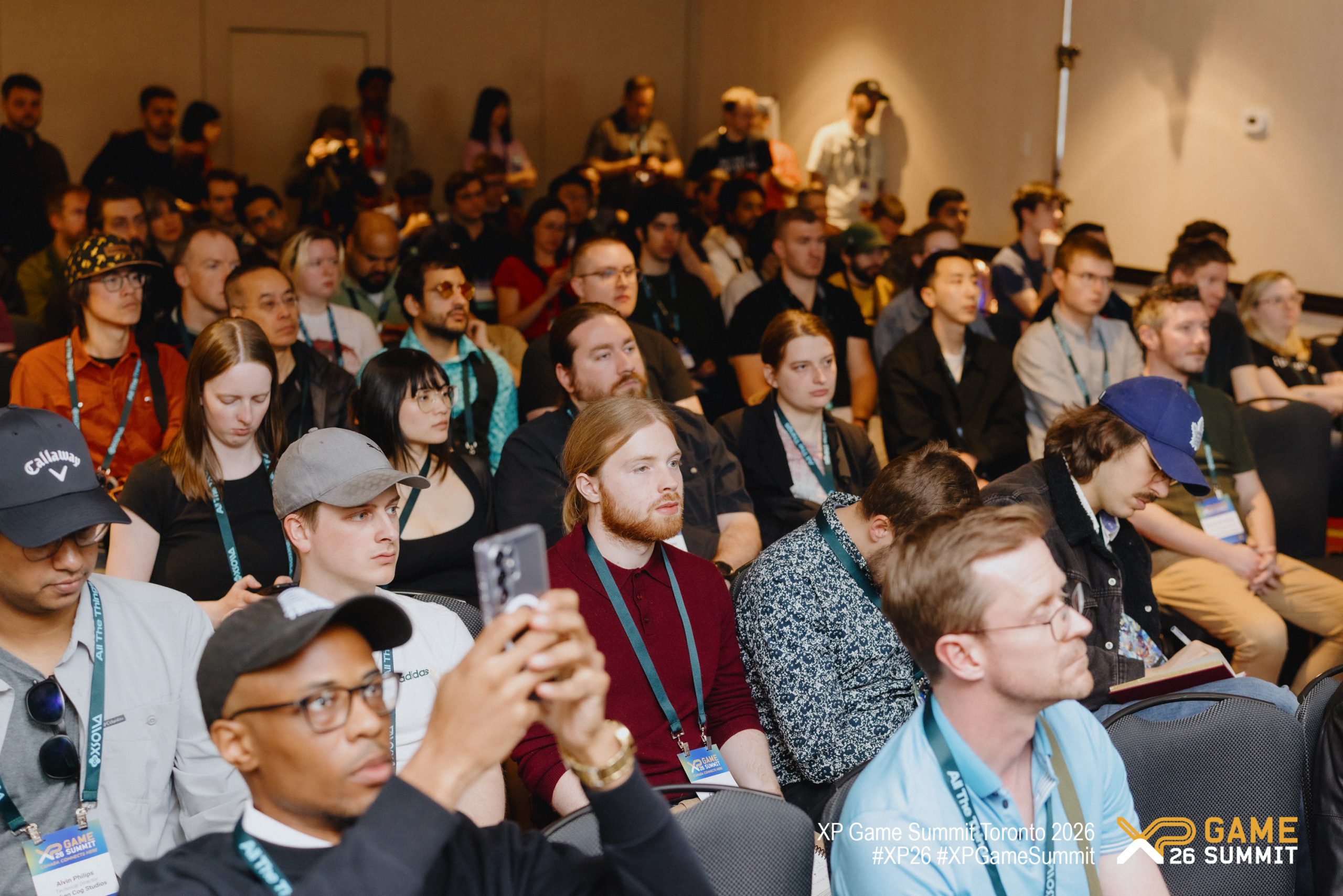 A diverse group of attendees sits attentively at the XP Game Summit Toronto 2026, with some taking notes and others capturing the moment on their smartphones.