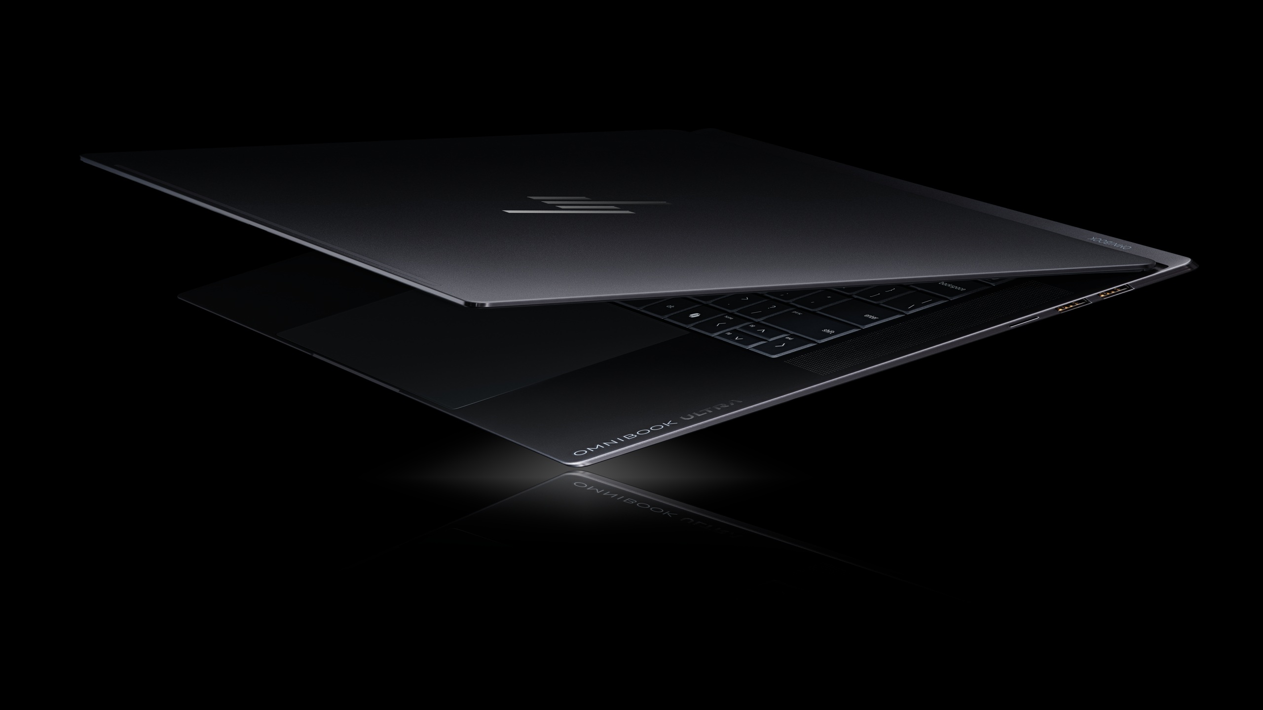 The partially open HP OMNIbook Ultra laptop is shown against a black background, highlighting its keyboard and sleek design.