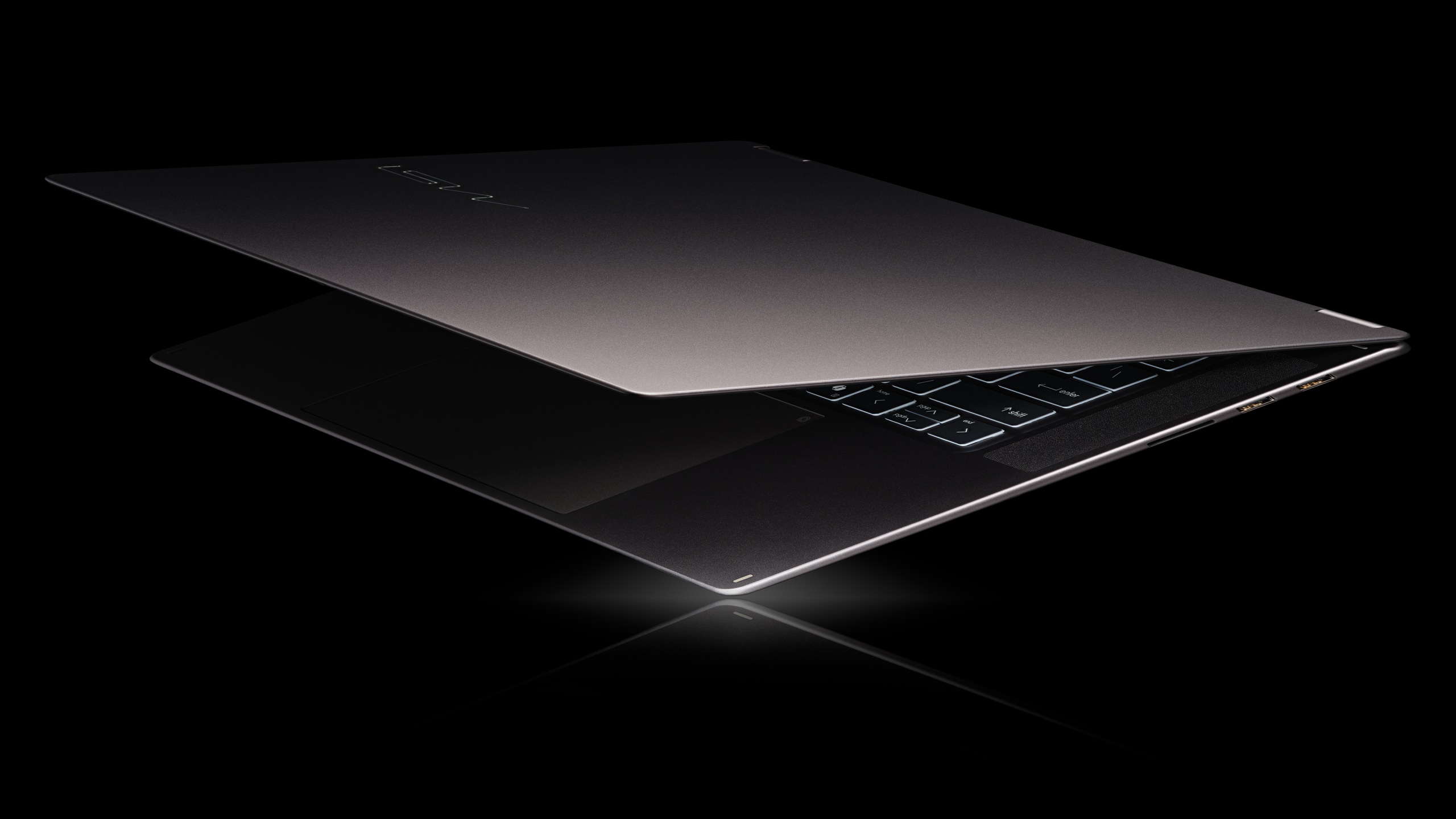 A partially open ASUS laptop with a visible illuminated keyboard against a black background.