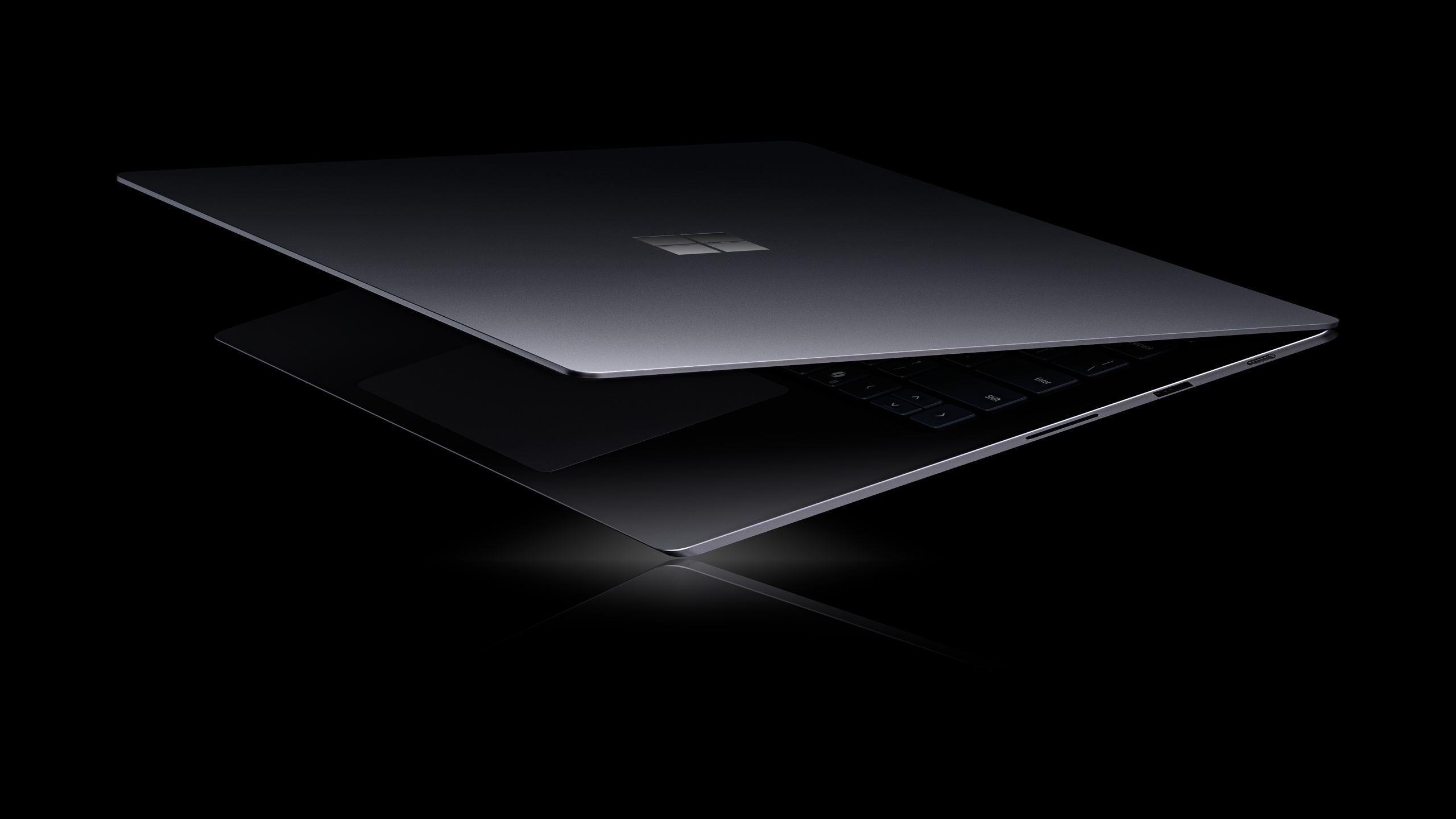 A partially open Microsoft Surface laptop with a reflective surface, displaying the Microsoft logo on a sleek black design.