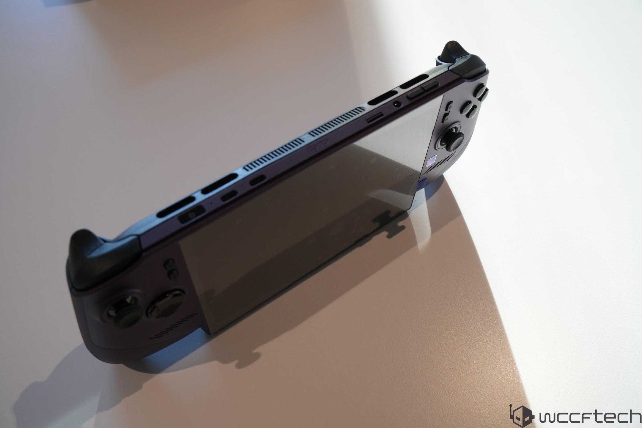 A handheld gaming console with a large display, featuring a visible joystick and buttons, resting on a white surface.