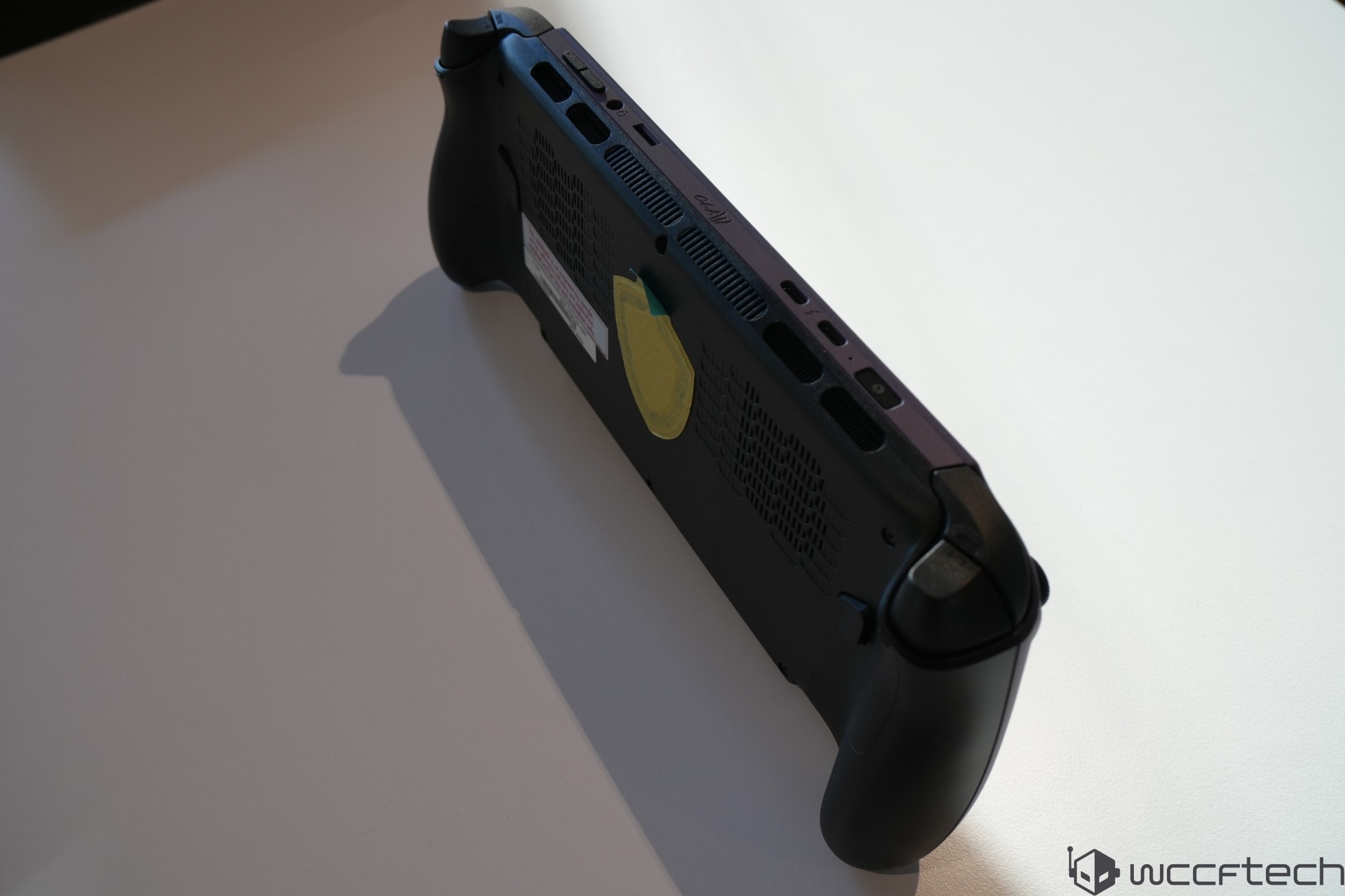 The underside of a handheld gaming device with cooling vents and control grips is shown on a white surface.