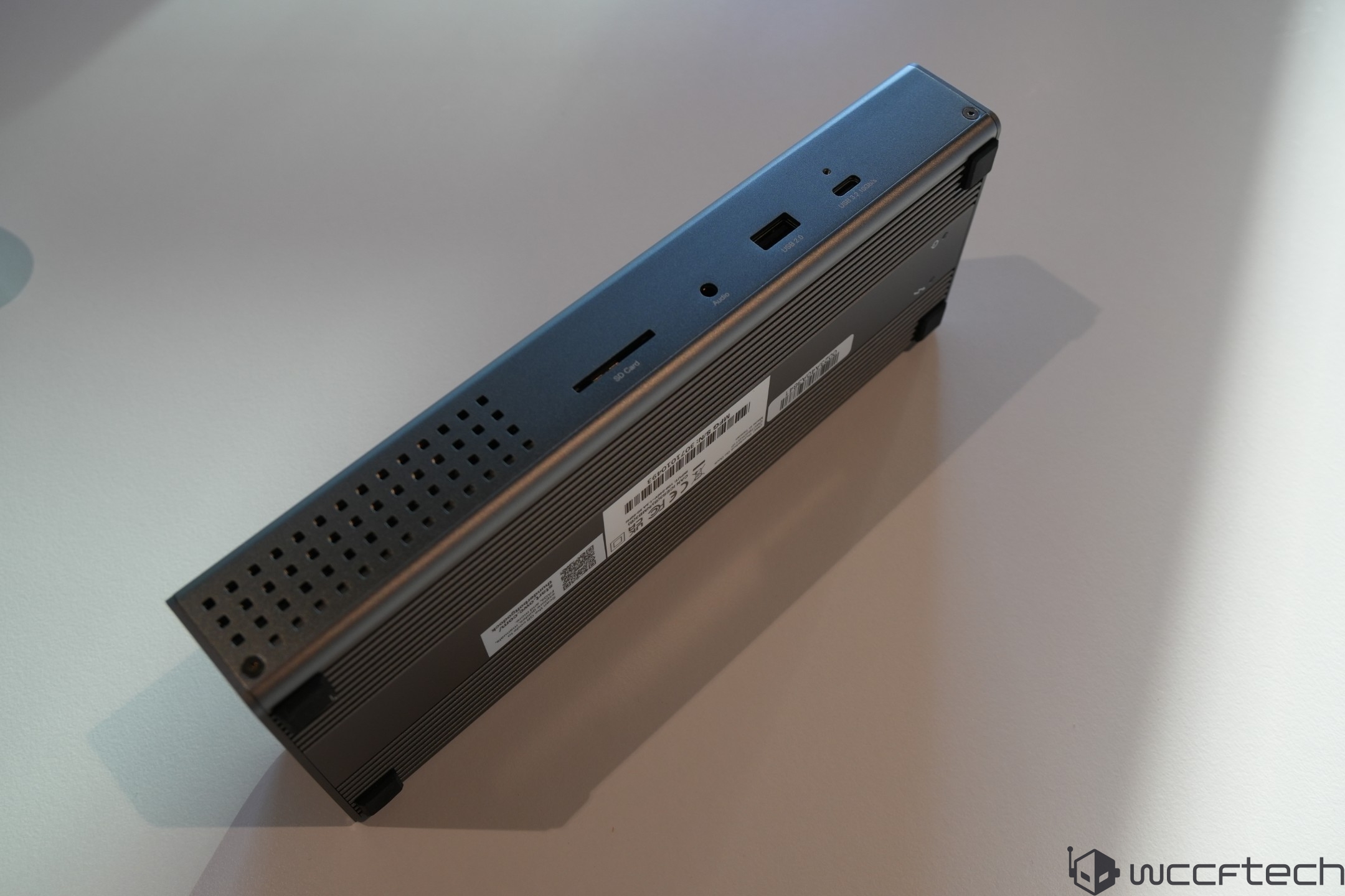 A rectangular unbranded mini PC with visible ports including 'SD Card,' USB, and a power button on a light gray surface.