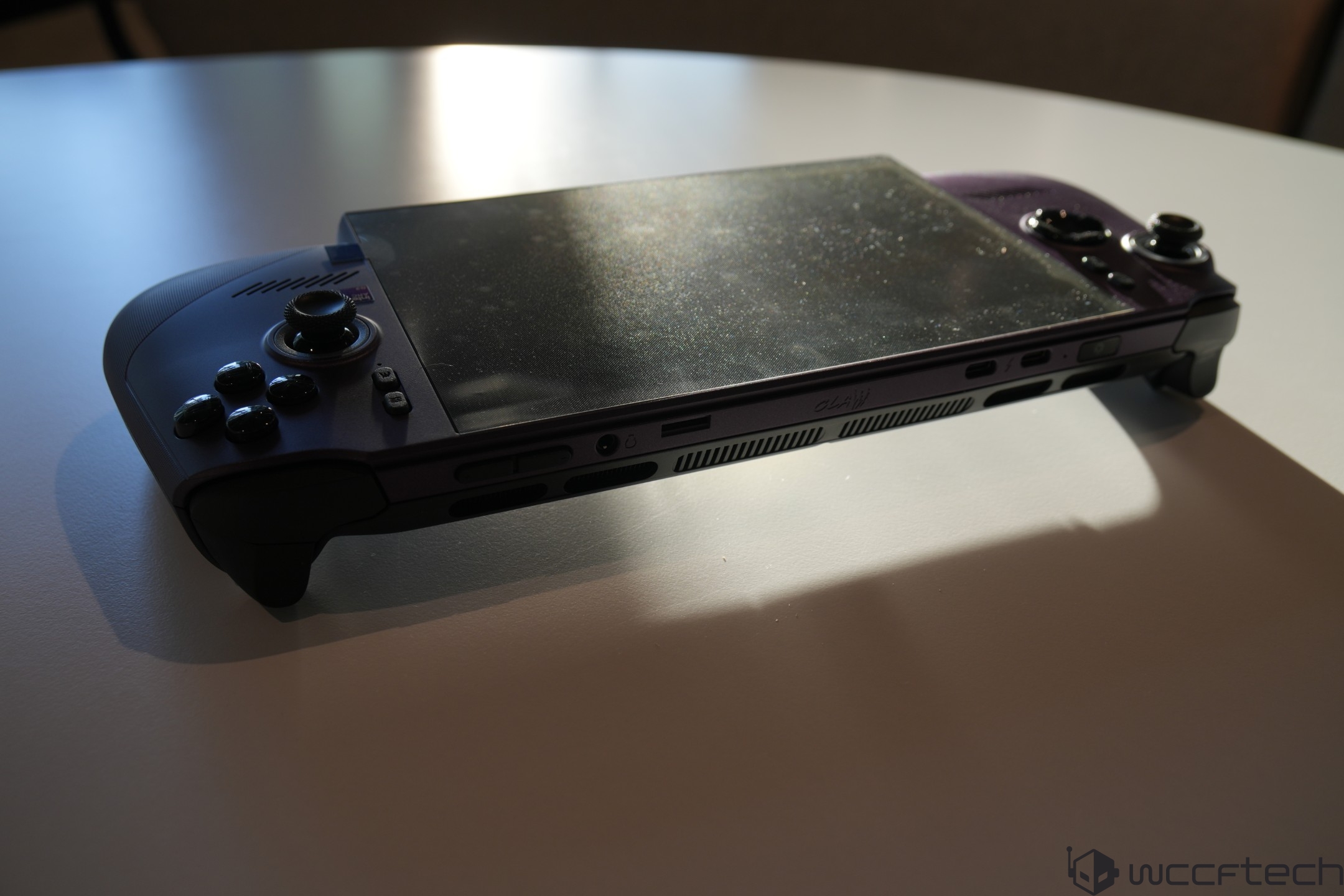 An unbranded handheld gaming console on a table, with visible joysticks and buttons, and the logo 'wccftech' in the bottom corner.