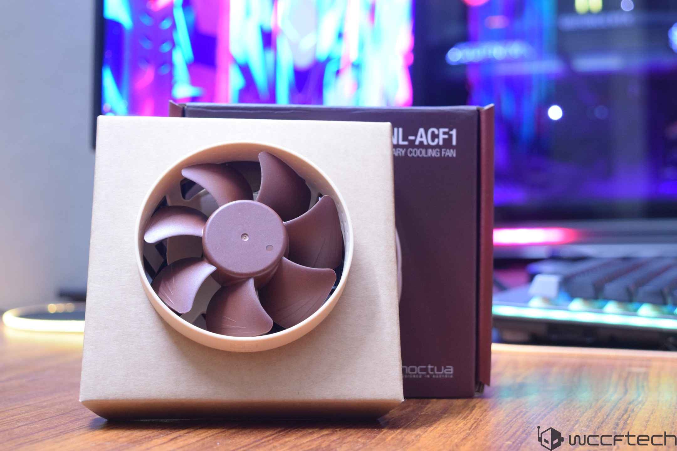 A Noctua NF-A6x25 FLX cooling fan is displayed in its packaging against a colorful gaming setup backdrop.