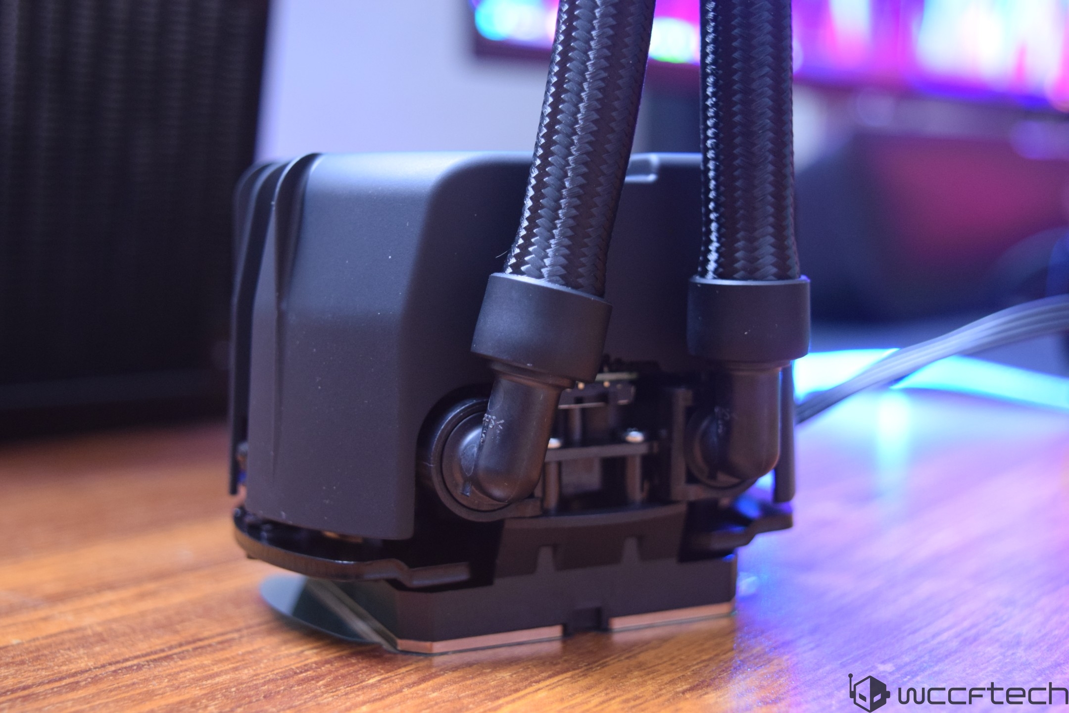 A close-up of an unbranded liquid cooling pump with braided tubes and visible connectors, resting on a wooden surface.