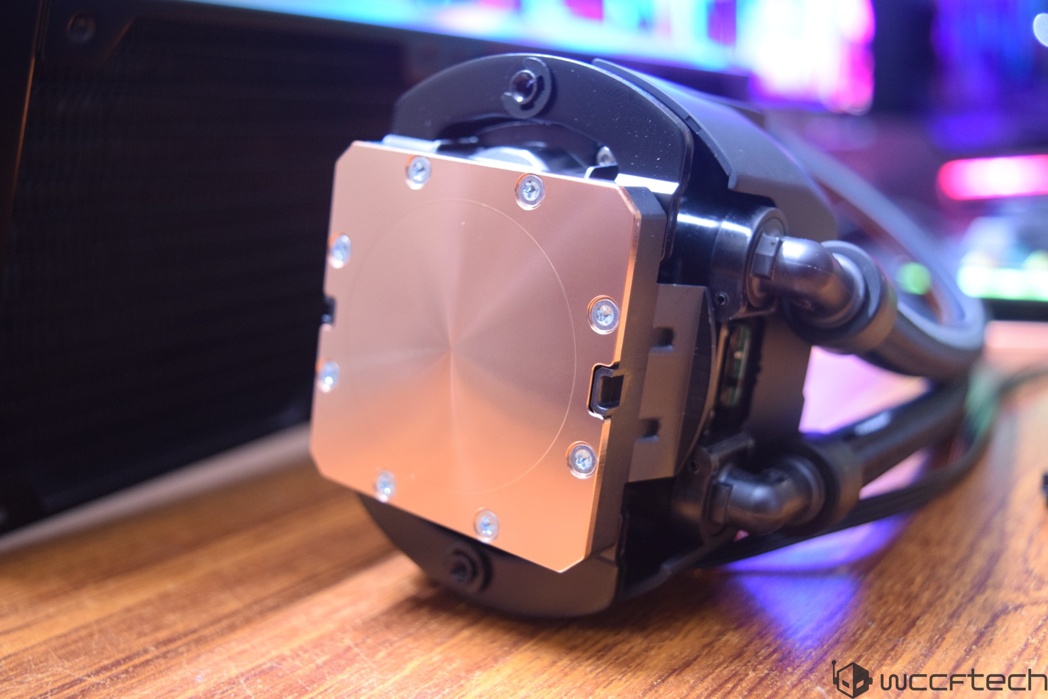 A close-up of an unbranded CPU cooler with a copper cold plate and dual hoses on a desk.