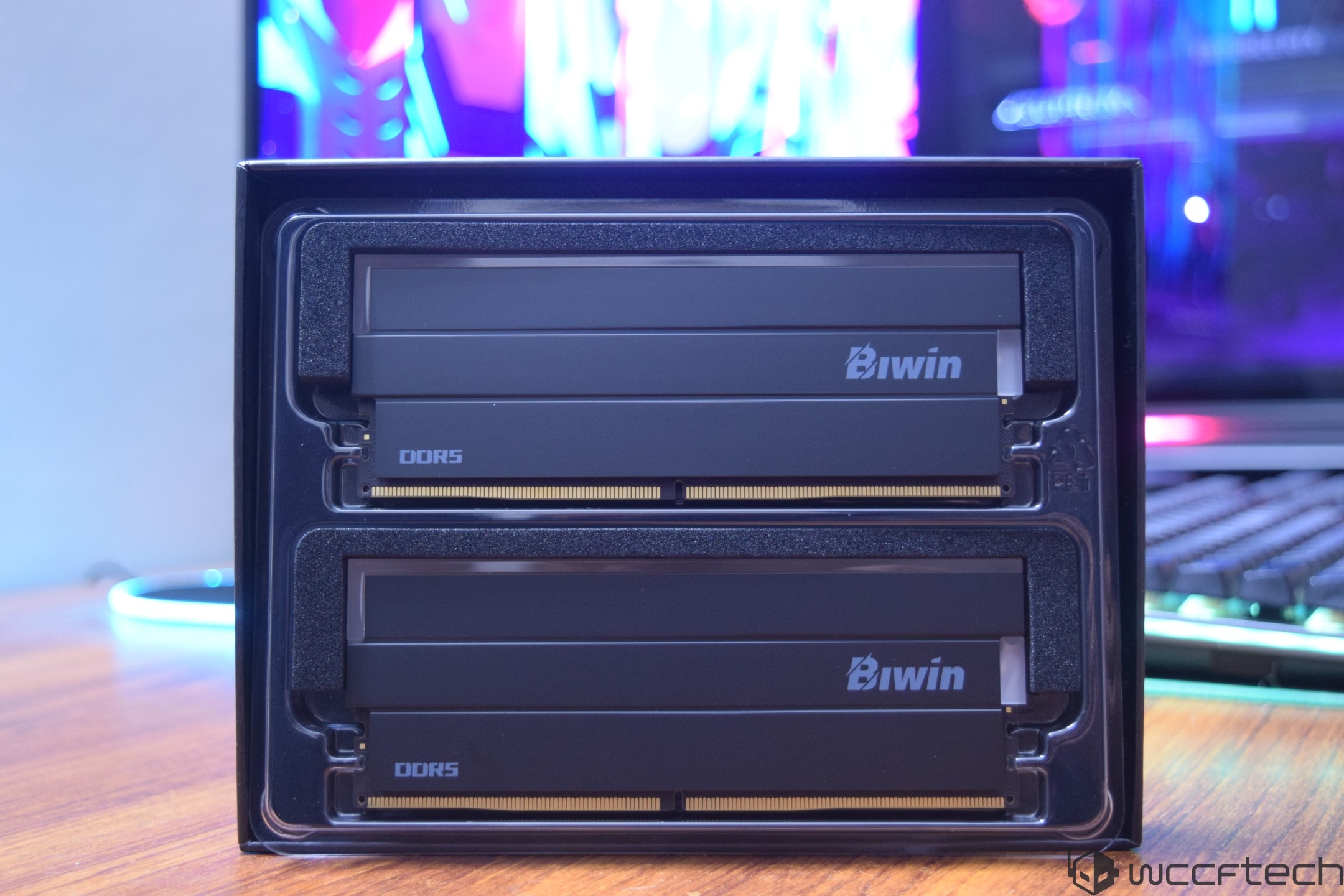 A close-up of two Biwin DDR5 memory modules in packaging, with a colorful, blurred background on a monitor.
