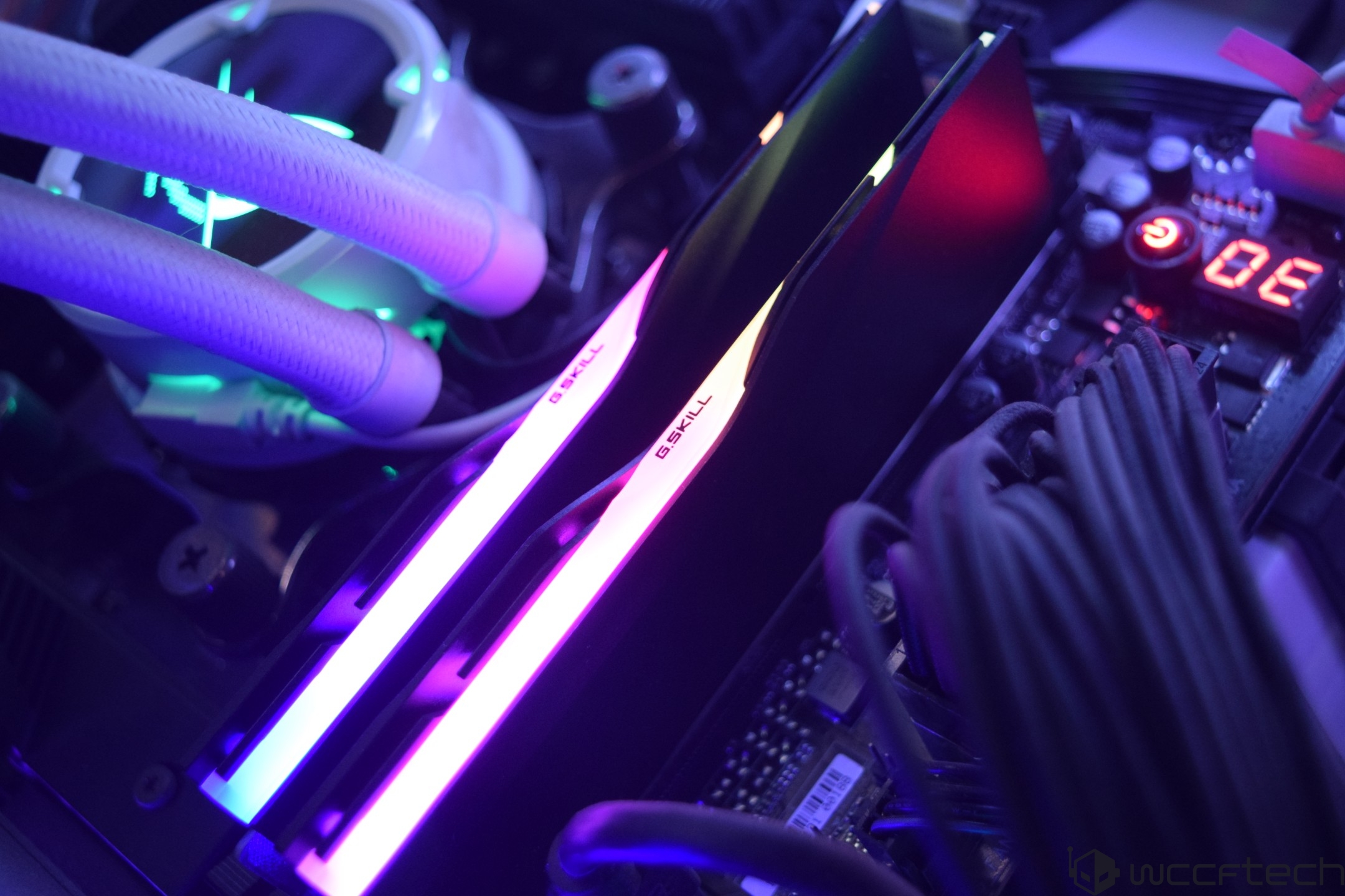 Two G.SKILL RAM sticks with RGB lighting are installed on a motherboard alongside CPU liquid cooling tubes and a visible '0E' diagnostic LED display.