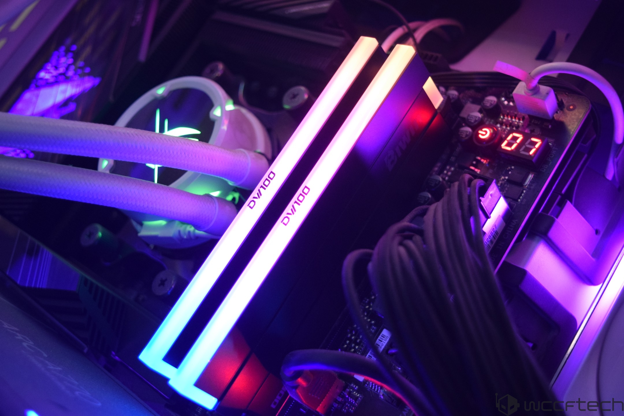Two sticks of RGB-illuminated RAM labeled 'DVI/100' are installed on a motherboard, alongside visible cooling tubes and a glowing digital display showing '87'.
