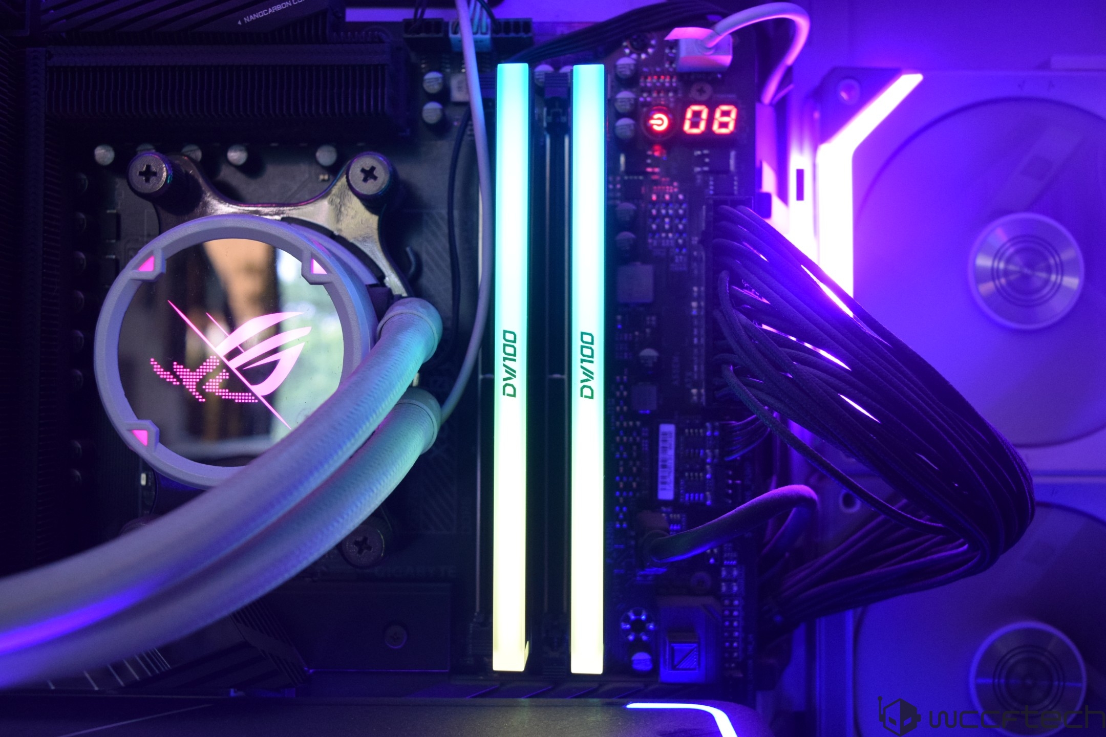 The image shows an ASUS ROG CPU cooler with a glowing logo next to two illuminated DIMM memory sticks labeled OVIDO on a motherboard inside a custom PC build.
