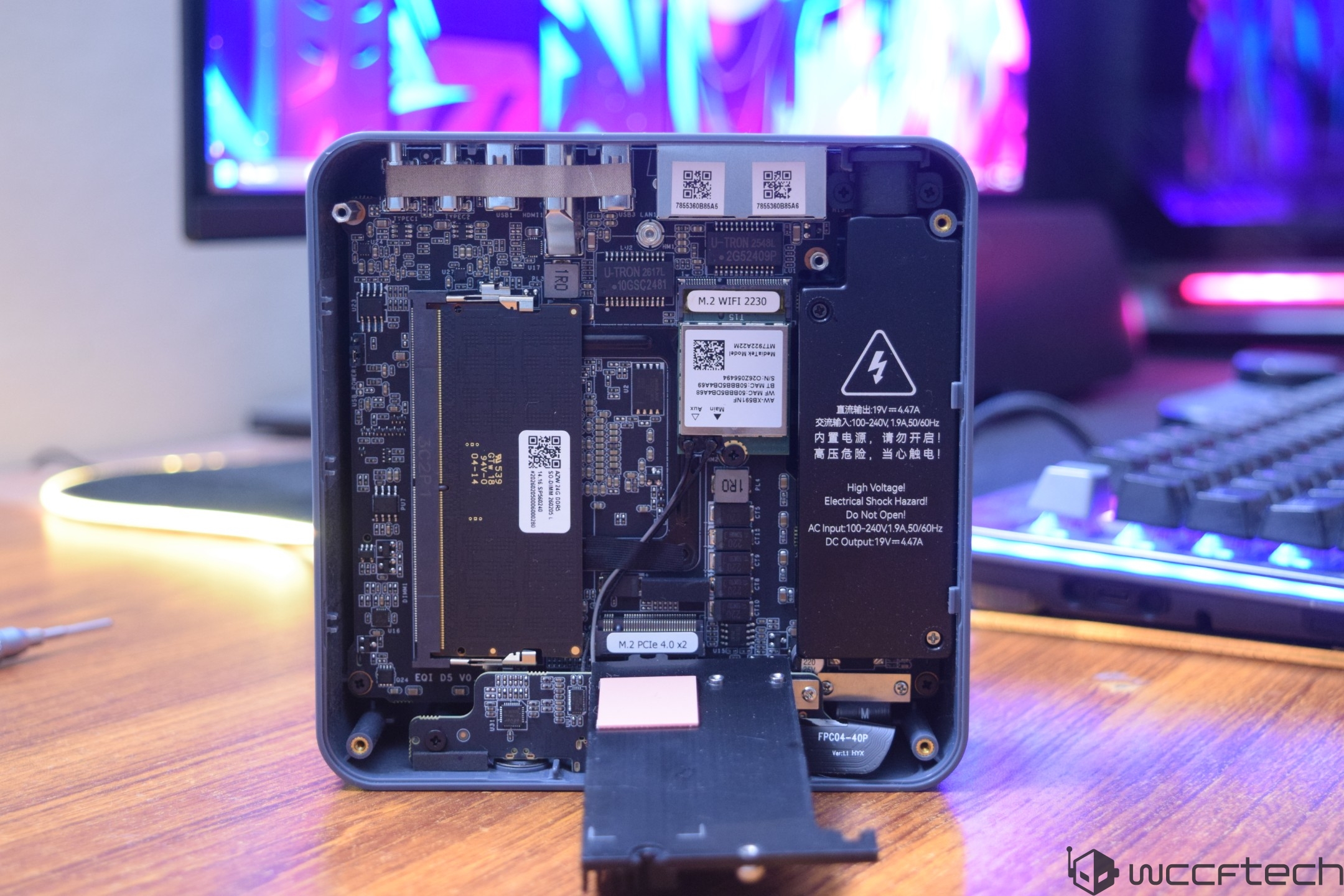 An open view of a Minisforum UN305 mini PC showing internal components, including M.2 WiFi 2230 and M.2 PCIe 4.0 x2 modules, with a warning label stating 'High Voltage Electrical Shock Hazard.'